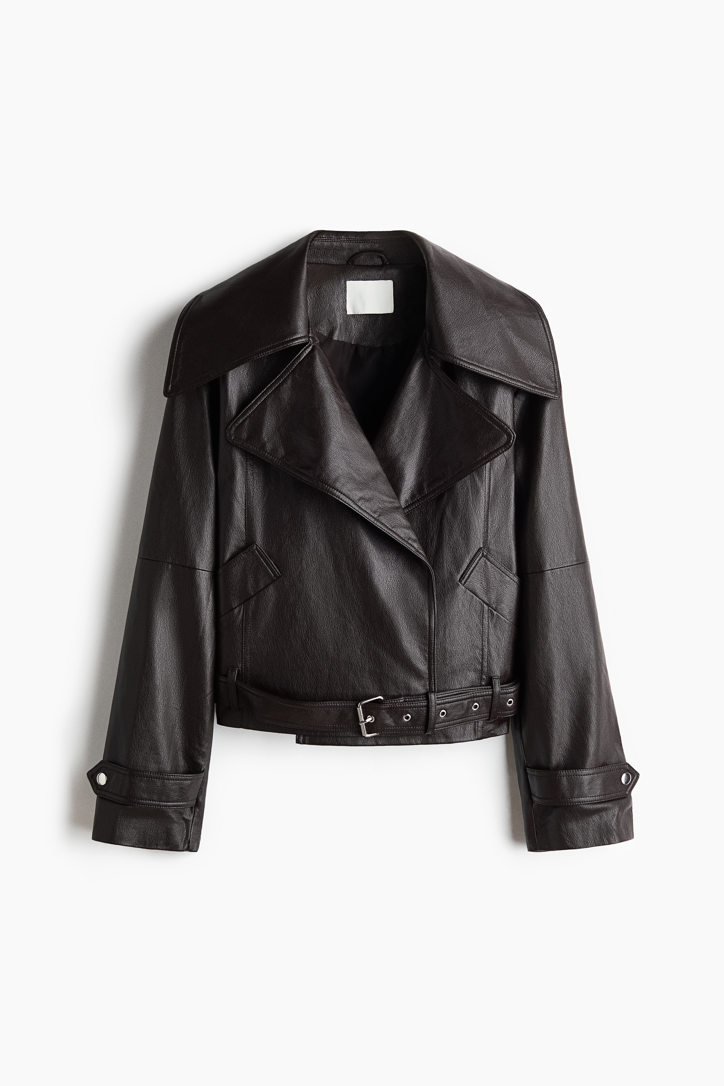 La modelo lleva una cazadora biker de gran tamaÃ±o en color marrÃ³n oscuro, con amplias solapas de muesca y un cinturÃ³n a juego con hebilla metÃ¡lica abrochado en el bajo. La cazadora se combina con una camisa celeste de cuello y unos vaqueros azules, junto con un vibrante jersey azul colocado sobre los hombros que la modelo estÃ¡ ajustando.