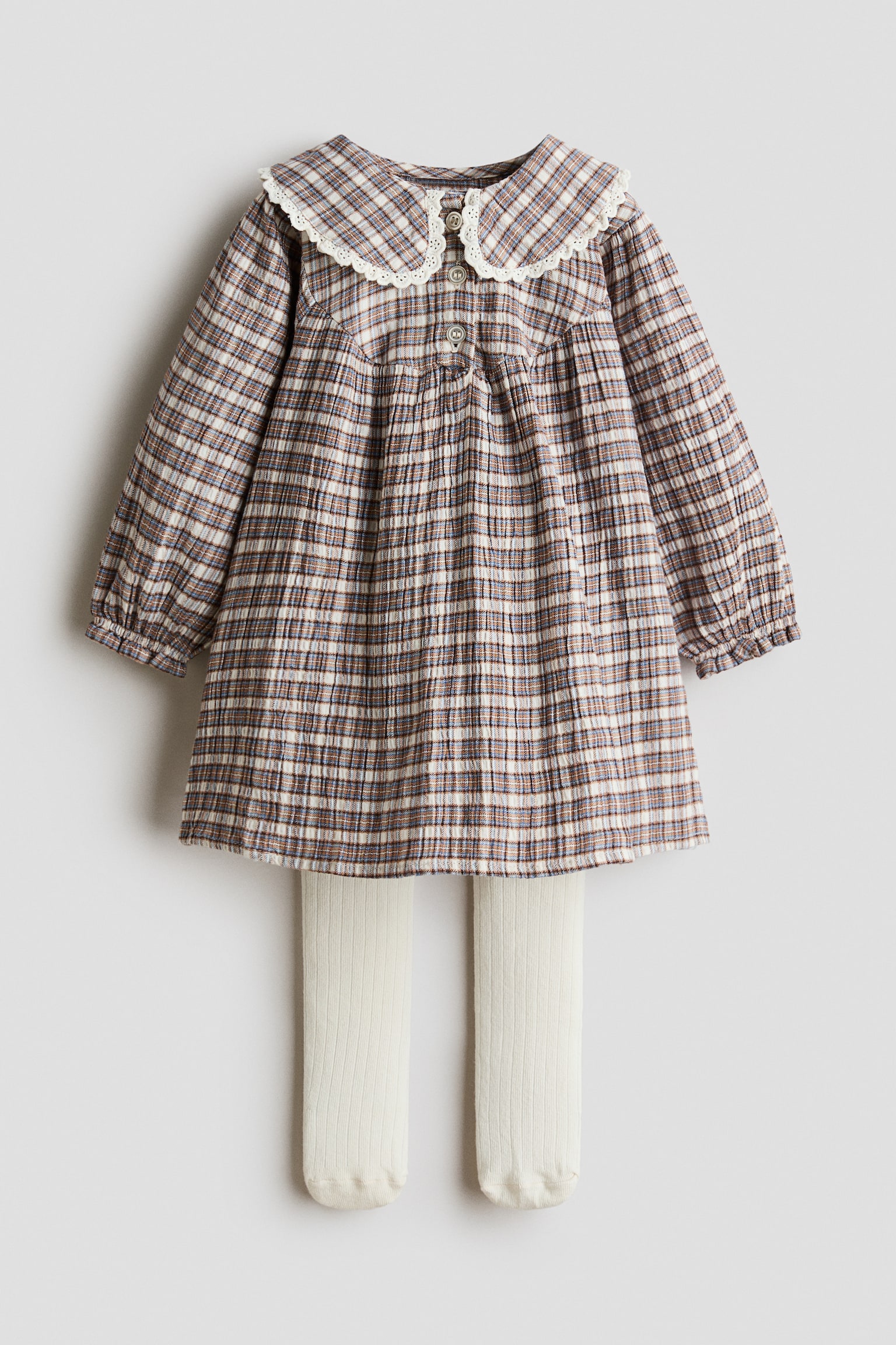 Un ensemble de robe pour enfant composÃ© dâune robe Ã  carreaux Ã  manches longues dans des tons marron, bleu et blanc, prÃ©sentÃ© de face, associÃ© Ã  des collants en maille cÃ´telÃ©e blanc cassÃ©. La robe prÃ©sente un large col Claudine avec finition en dentelle blanche, une patte de boutonnage sur le devant et des poignets volantÃ©s Ã©lastiquÃ©s.