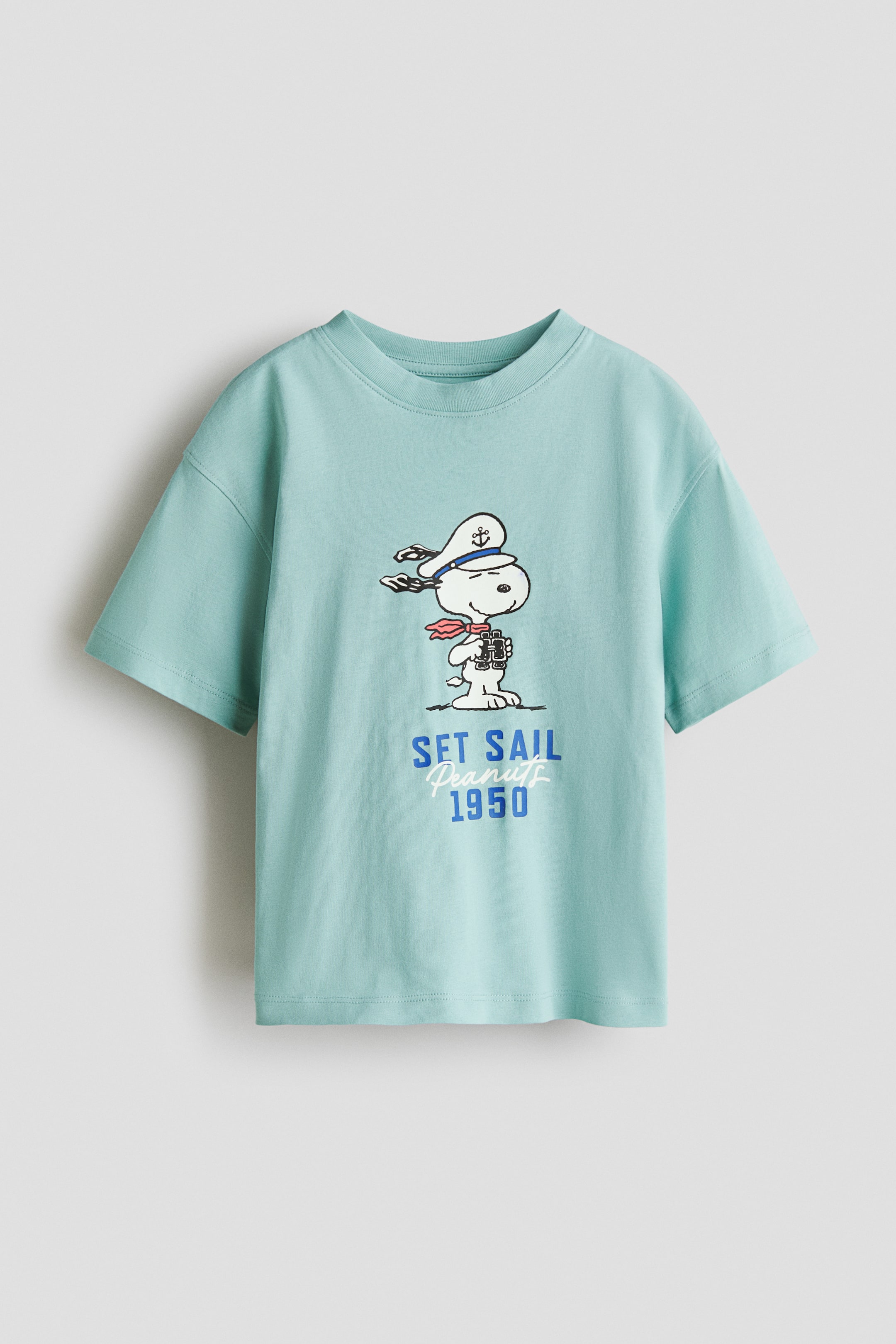 View larger image: The oversized t-shirt, displayed from the front, is a light blue printed cotton jersey showcasing a graphic of Snoopy as a sailor peering through binoculars along with the text "SET SAIL Peanuts 1950". It is crafted with a ribbed neckline and features dropped shoulders.