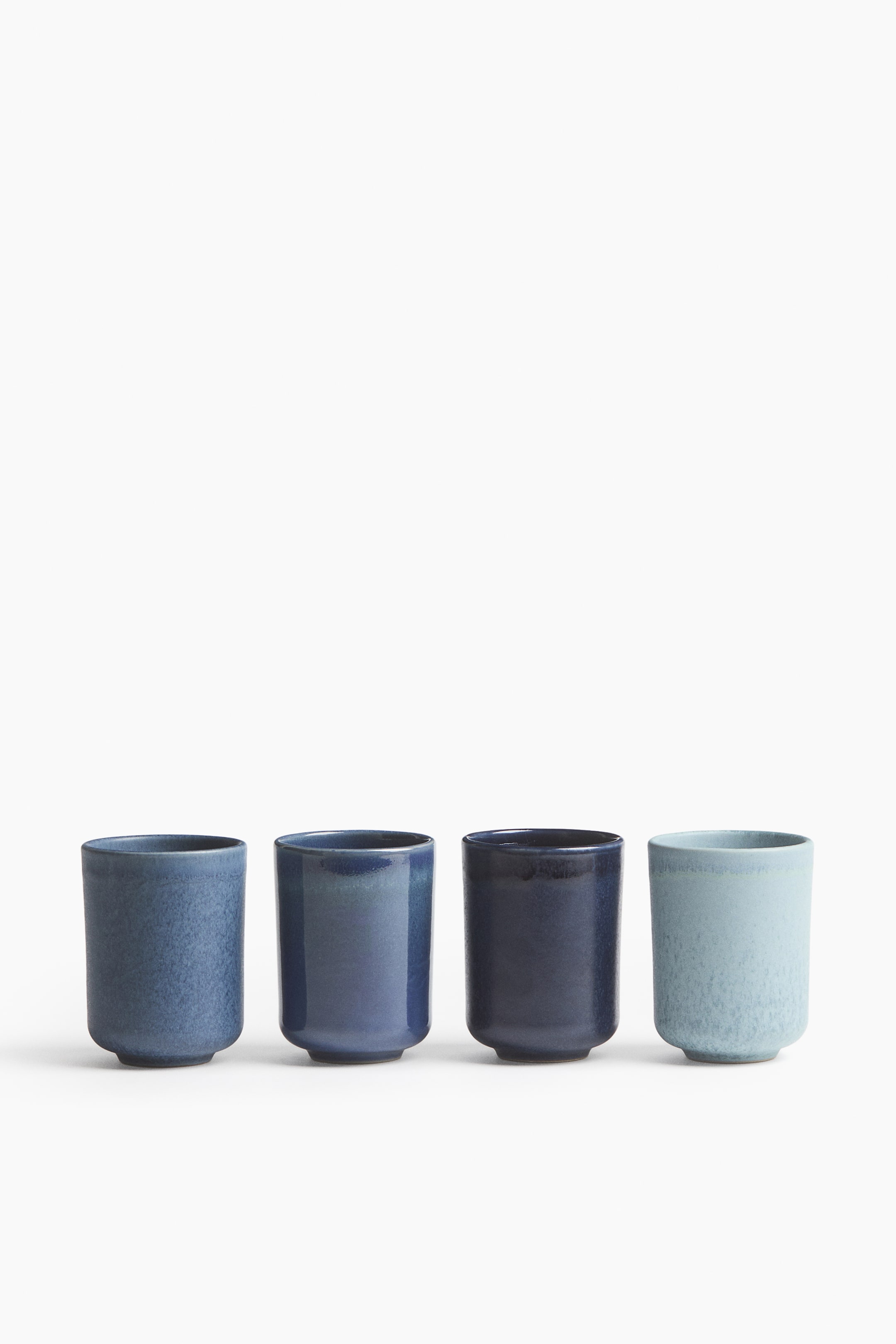 Visualizza immagine più grande: Quattro tazze in gres senza manico sono disposte in fila, rivolte frontalmente, e mettono in risalto assortite smaltature blu e finiture materiche. I pezzi presentano variazioni uniche di colore e texture, che vanno da un azzurro chiaro punteggiato con finitura opaca a un blu navy intenso con smalto lucido.