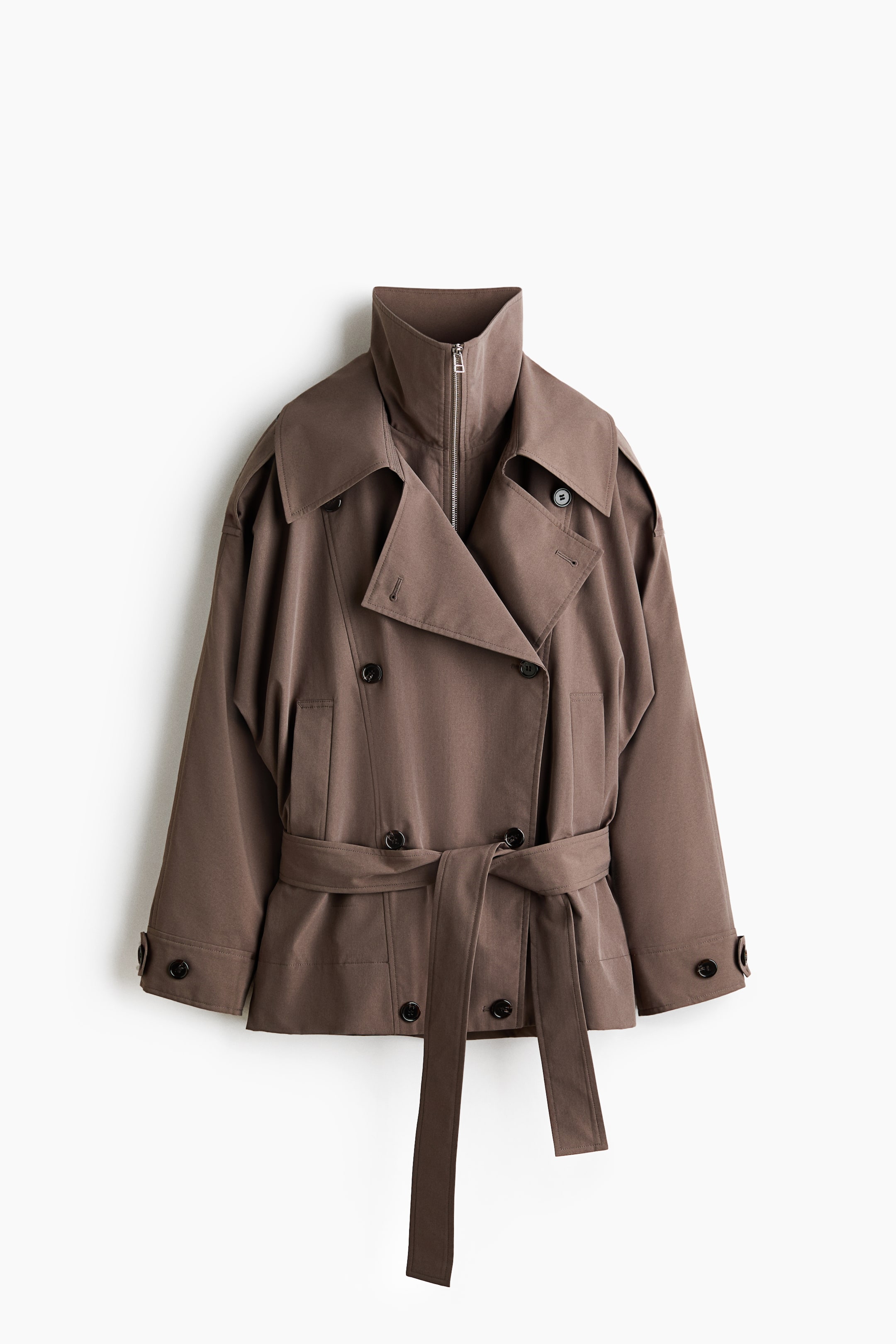 View larger image: A muted brown short trench coat is shown from the front, featuring a double-breasted design with dark buttons. It showcases a layered collar with an inner stand collar and zippered closure, wide trench lapels, shoulder epaulets, and cuffed sleeves with button tabs, while a matching fabric belt is tied at the waist.