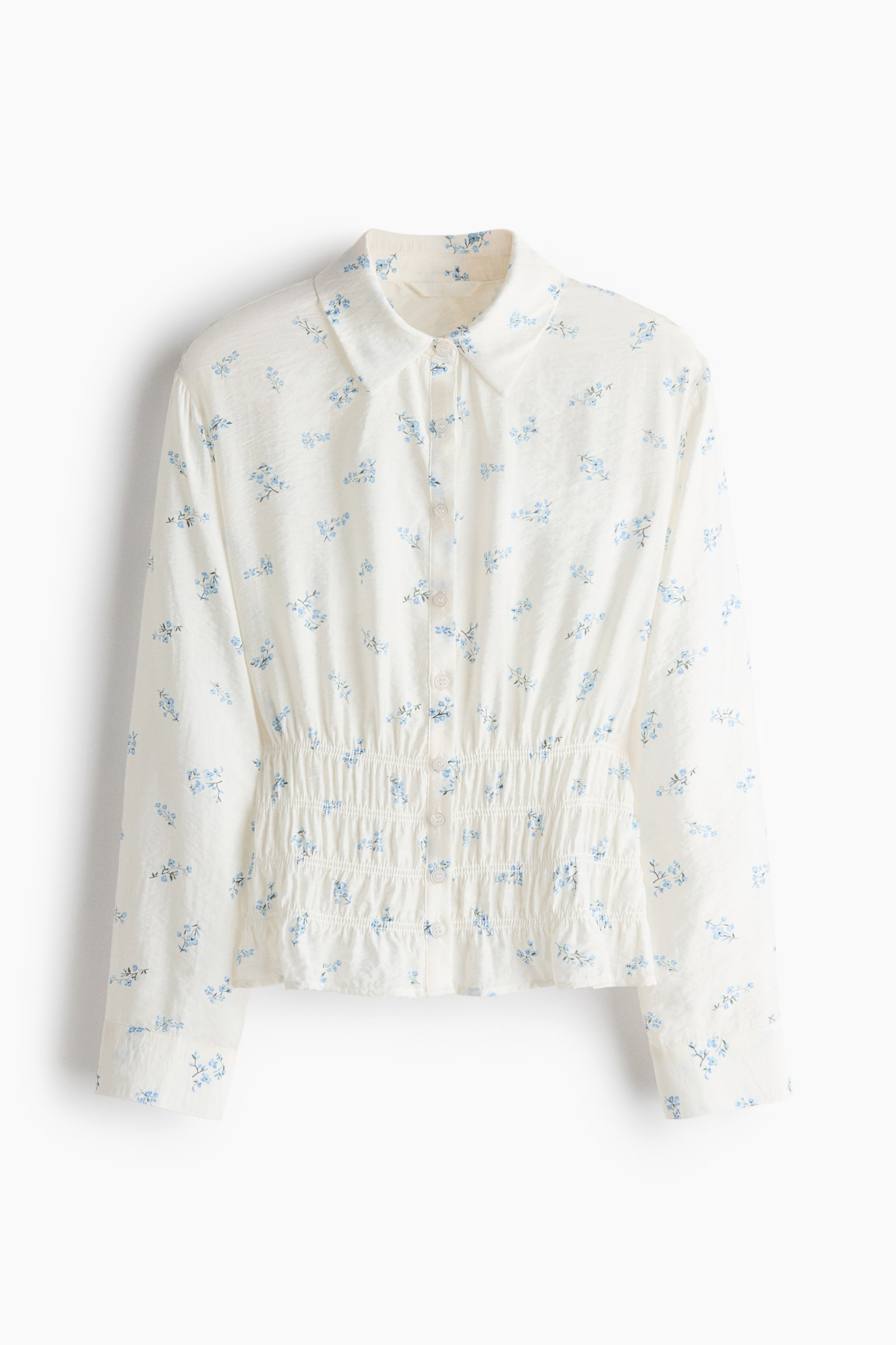 A cream-coloured blouse featuring a delicate blue floral print is shown from the front, displaying a classic collar, a button-down front, and long sleeves with buttoned cuffs. The design showcases a wide, smocked elasticated waist that creates a cinched silhouette. - 1