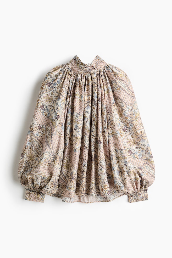 Cette vue de face présente une blouse surdimensionnée en tissu tissé, ornée dâun imprimé paisley multicolore complexe. La blouse met en valeur un col montant haut froncé avec des fronces à la base, se déployant dans une silhouette volumineuse avec de longues manches ballon raglan et de larges poignets. - 1
