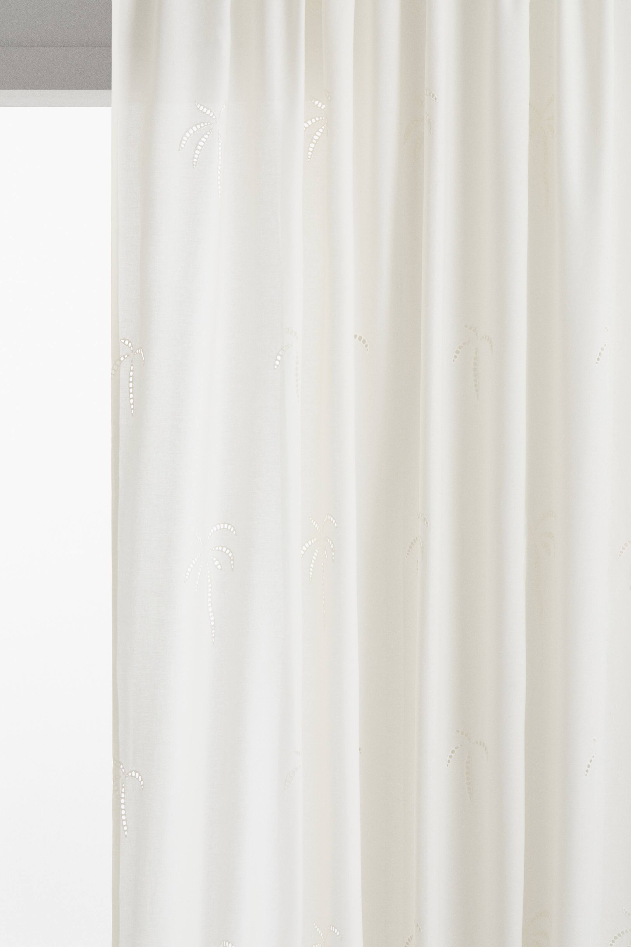 View larger image: The front of the off-white curtain showcases a repeating pattern of perforated palm tree shapes. It hangs in soft vertical folds.