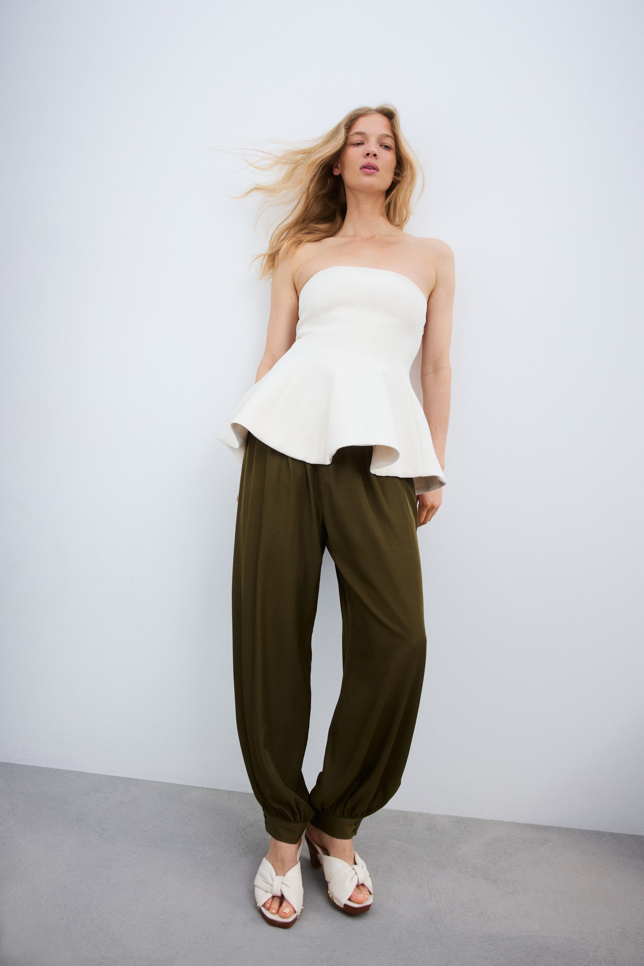 Größeres Bild ansehen: Ein weißes, trägerloses Peplum-Top mit einem eng anliegenden Oberteil und einem strukturierten Peplum-Saum, der von der Taille aus ausgestellt ist.