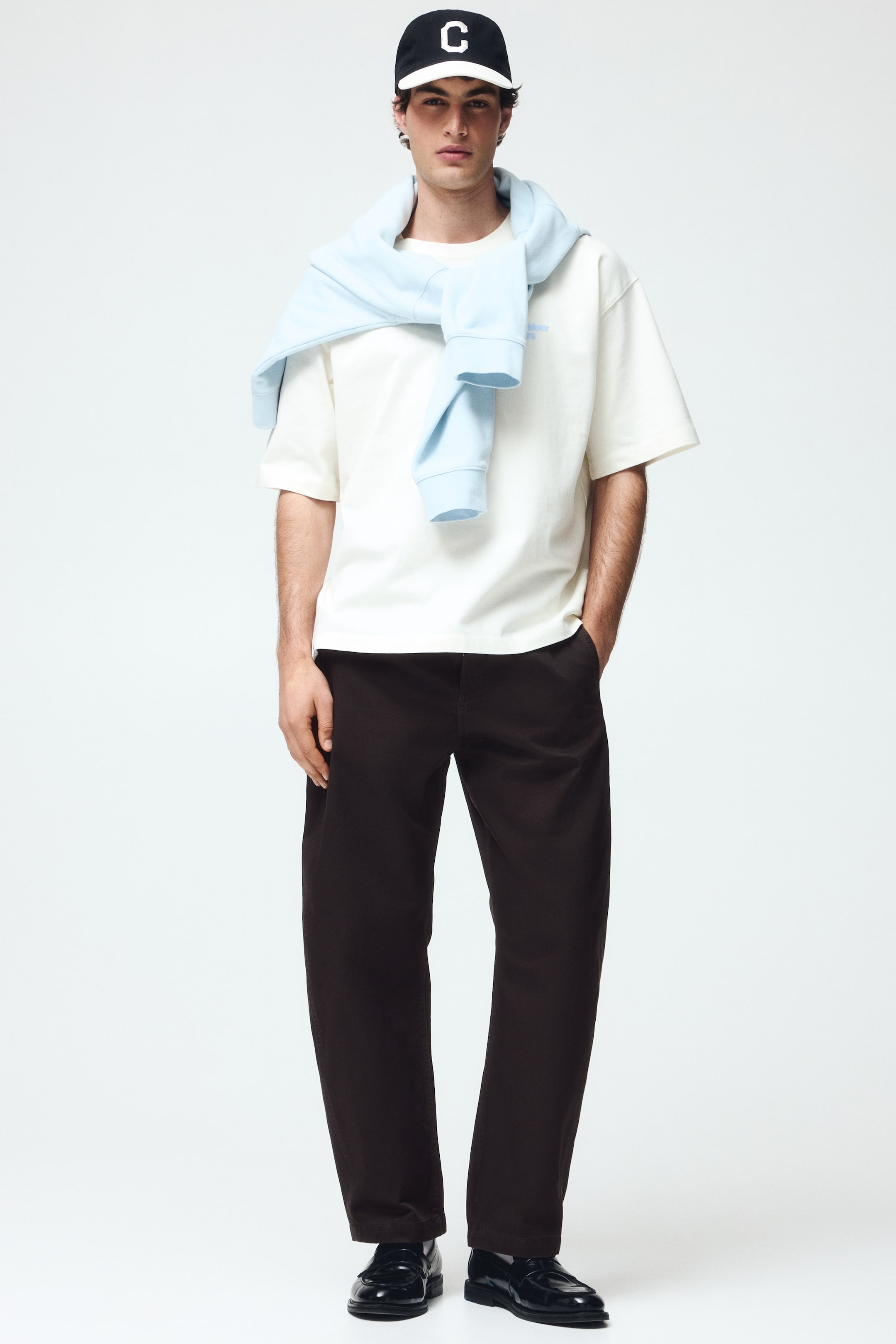 View larger image: Dark brown trousers are showcased from a front-facing angle, featuring a relaxed, straight-leg fit. Side pockets are visible, and the hem rests just above black loafers, highlighting their full length.