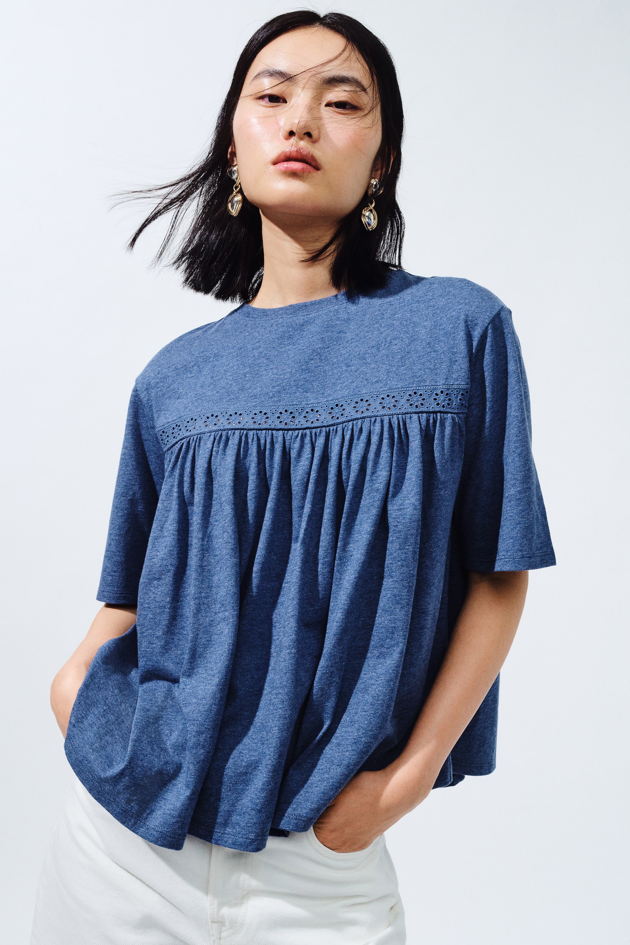 View larger image: The heathered blue short-sleeved top features a crew neck and an eyelet-lace panel across the chest. Gathers create a loose, flowing fit below the panel.