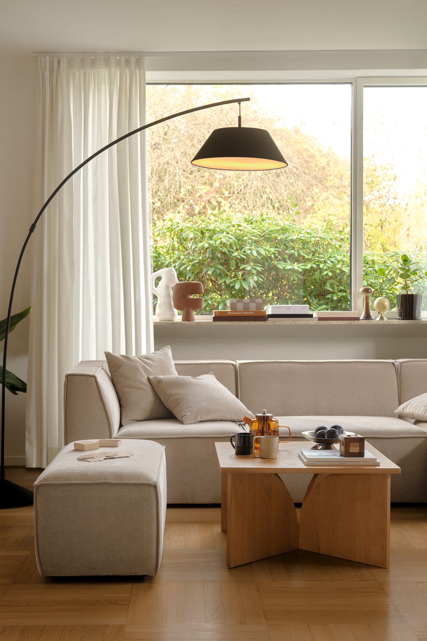 Ein modulares Dreiteiler-Sofa ist nach vorne ausgerichtet und zeigt ein flaches, kantiges Design, bezogen mit einem strukturierten, hellbeigen Stoff. Das Sofa verfÃ¼gt Ã¼ber einen mittleren, armlehnenlosen Abschnitt, der von zwei Endelementen mit breiten, integrierten Armlehnen flankiert wird, die in die RÃ¼ckenlehne Ã¼bergehen.