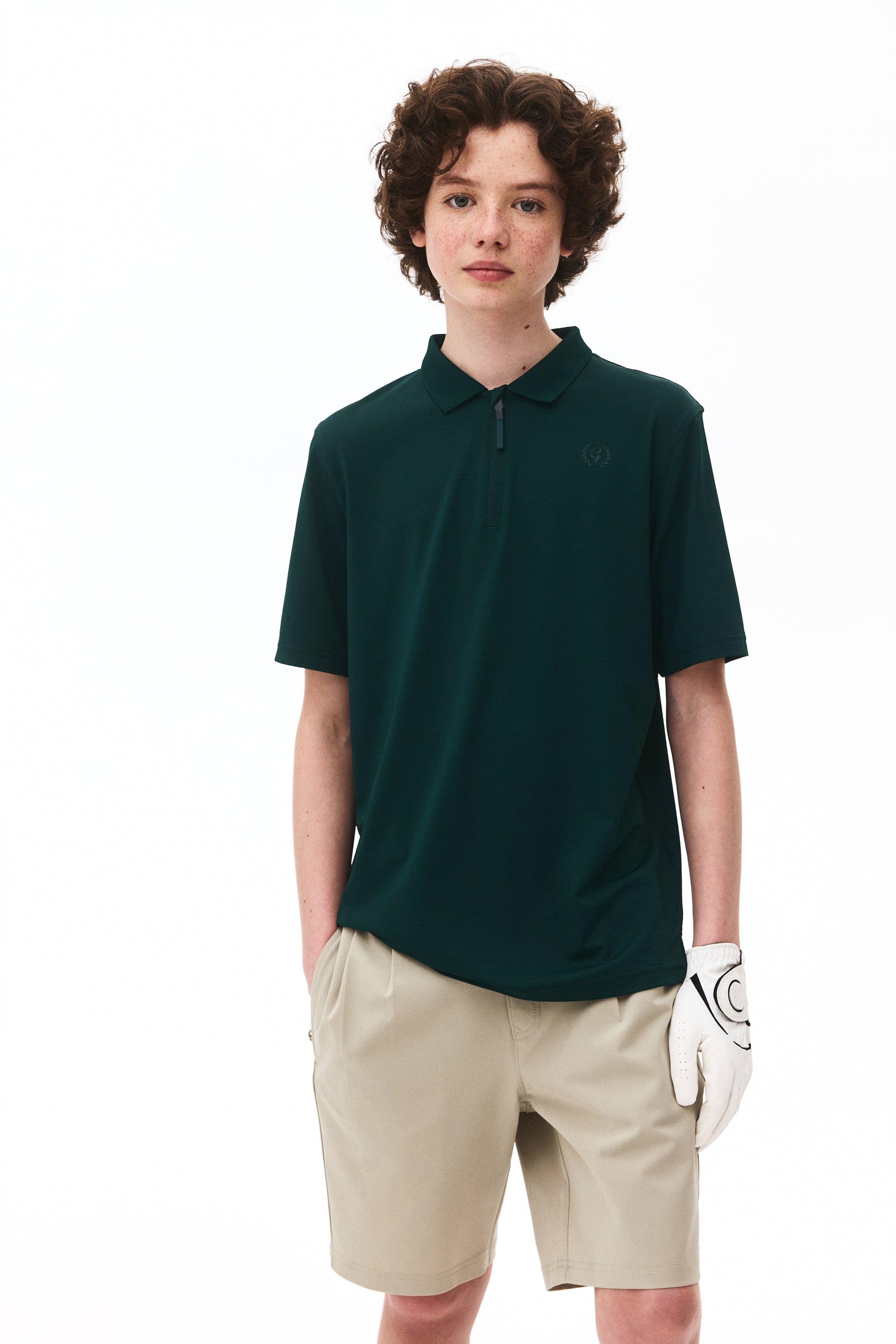 View larger image: A dark green polo shirt featuring a collar, a quarter-zip placket, and short sleeves. An embroidered crest is visible on the left chest, and the fabric shows a subtle textured pattern.