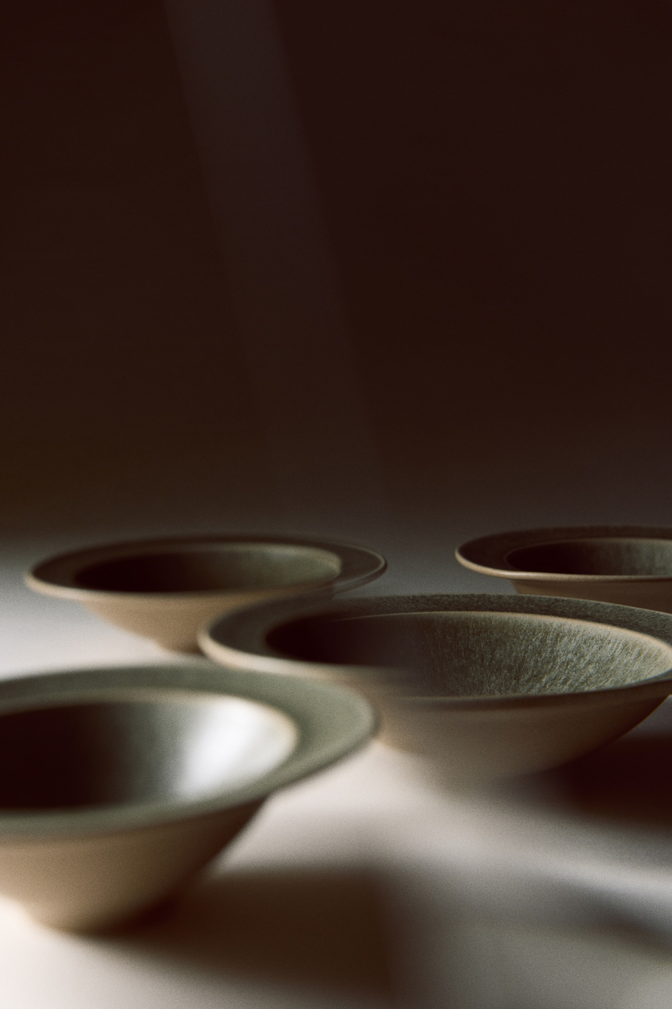 Größeres Bild anzeigen: Vier tiefe Steingutteller mit klassischem breitem Rand liegen zusammen und zeigen innen eine strukturierte, grünlich-graue Reaktivglasur sowie außen ein mattes, natürliches Beige-Finish.