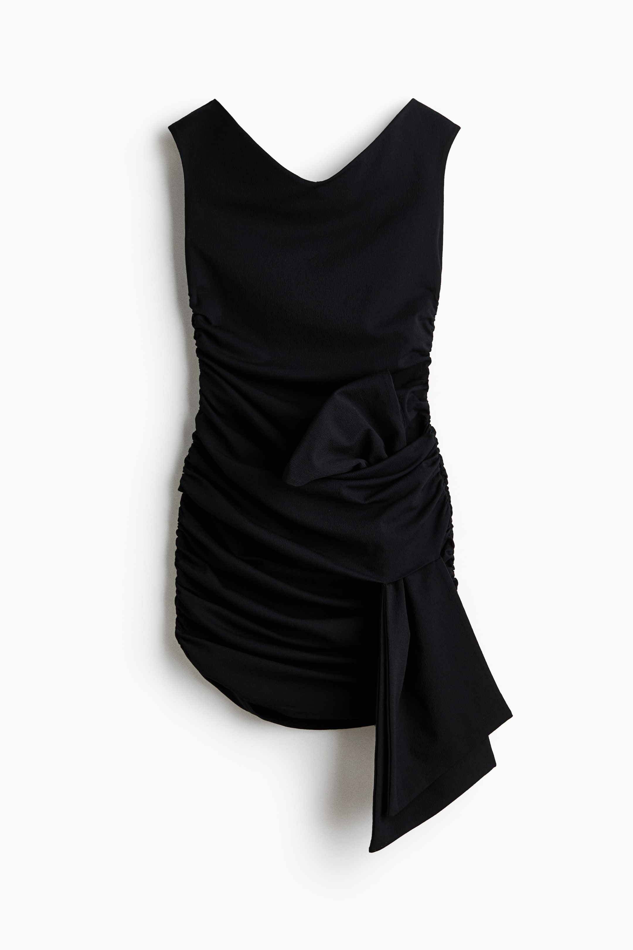 View larger image: A black sleeveless dress featuring a V-neckline and extensive ruching along the sides and front. A large fabric bow adorns the front, with an asymmetrical draped panel extending from it towards the right.