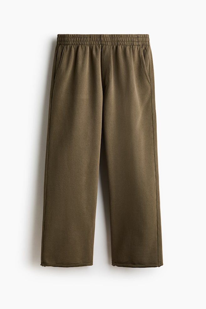 Olive green pants are laid flat, showcasing a relaxed, straight-leg fit with an elastic waistband and two slanted side pockets. - 1