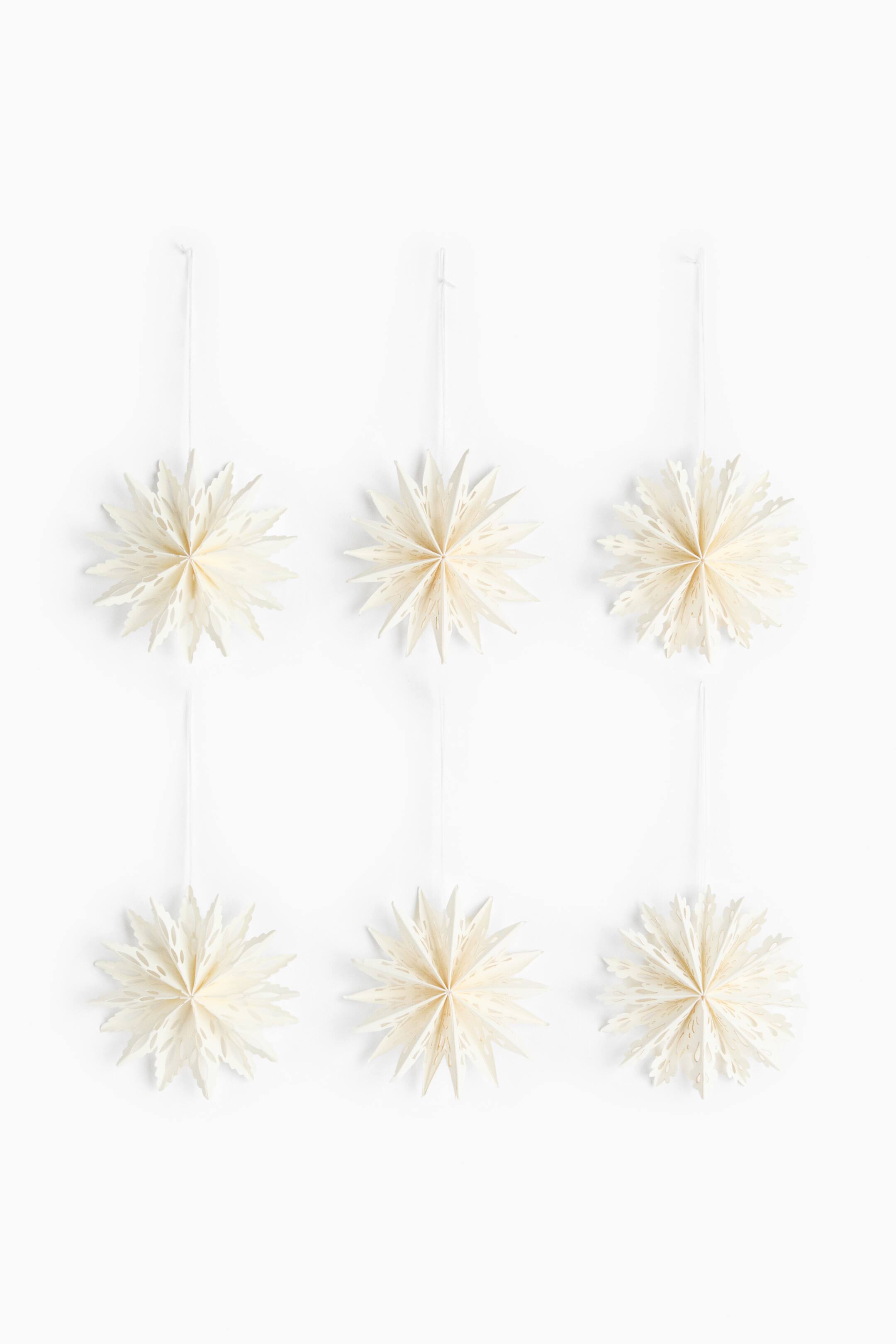 View larger image: Six cream-colored paper star ornaments hang in a two-by-three grid, shown from a front angle. Each three-dimensional star features multiple folded points with delicate cutout patterns and hangs from a thin white string.