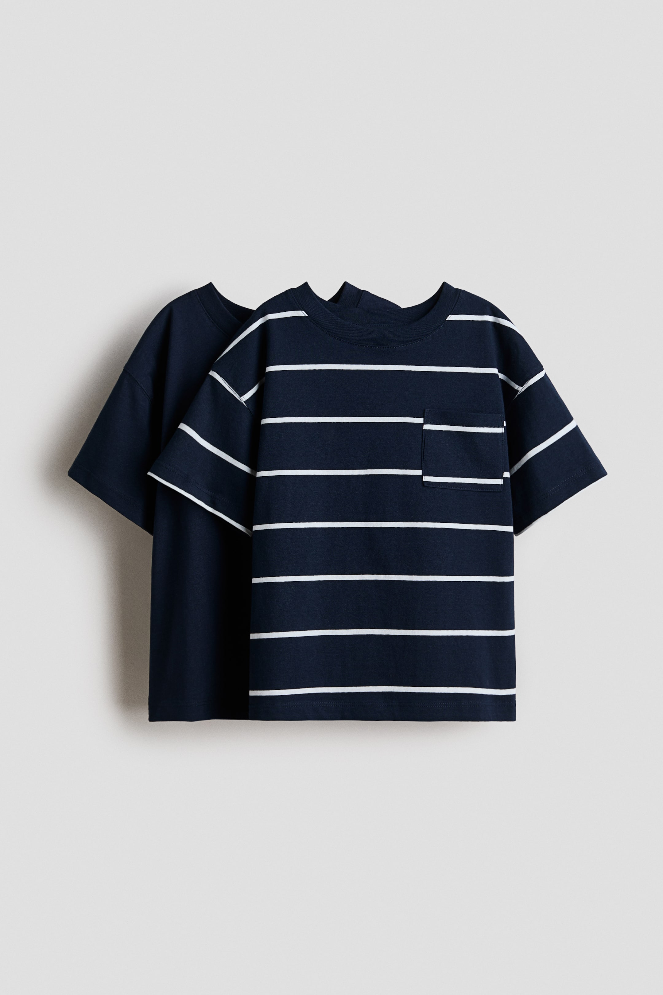 View larger image: Two T-shirts are shown from the front: a navy-blue T-shirt with white horizontal stripes, a crew neck, short sleeves and a chest pocket sits in front, with a solid navy-blue T-shirt layered behind it.