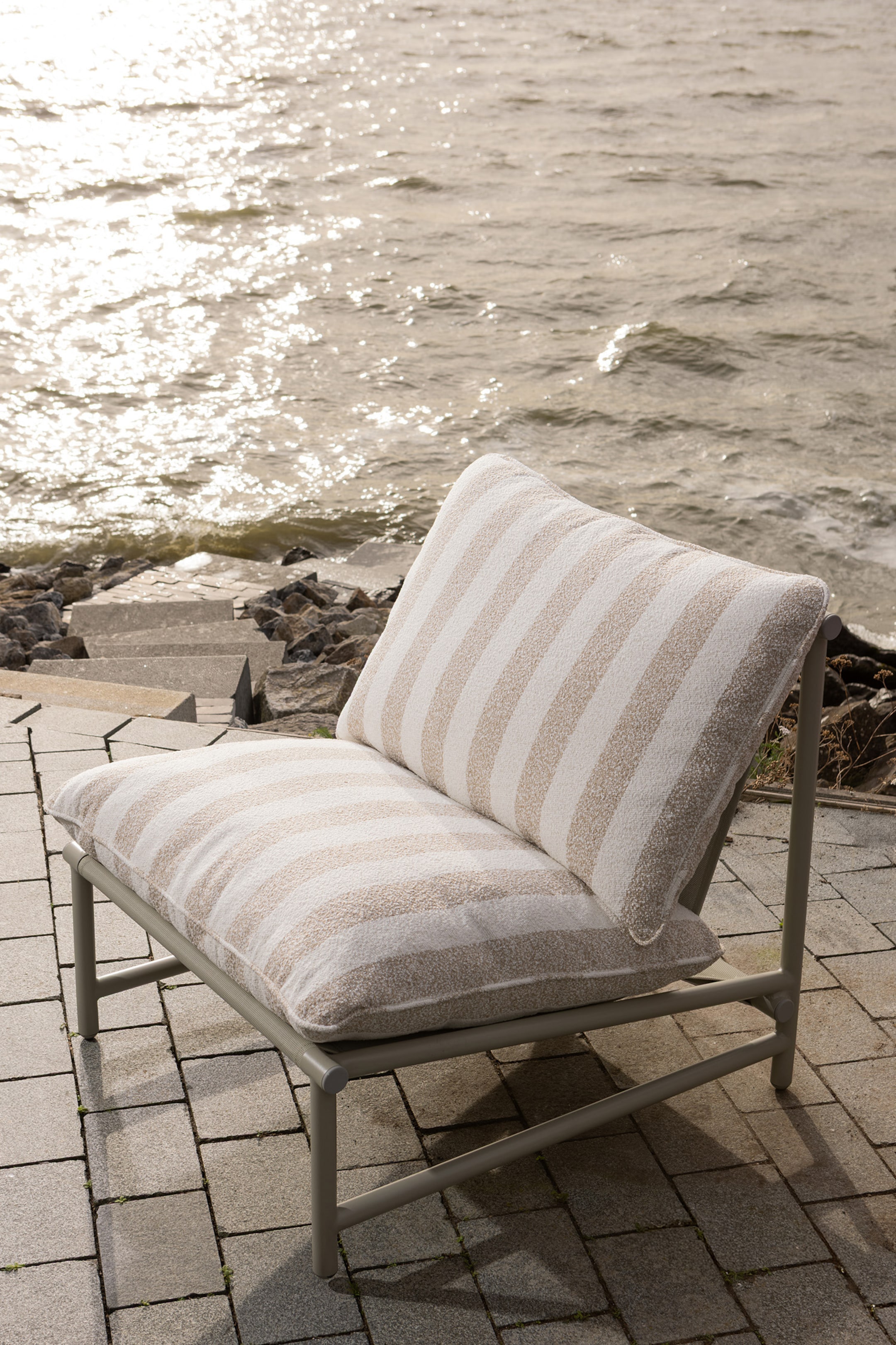 Agrandir l'image: Une chaise longue d'extérieur est dotée d'une structure en métal gris clair et de deux coussins épais. Les coussins de siège et de dossier présentent des rayures horizontales alternées en tissu beige texturé et blanc cassé.
