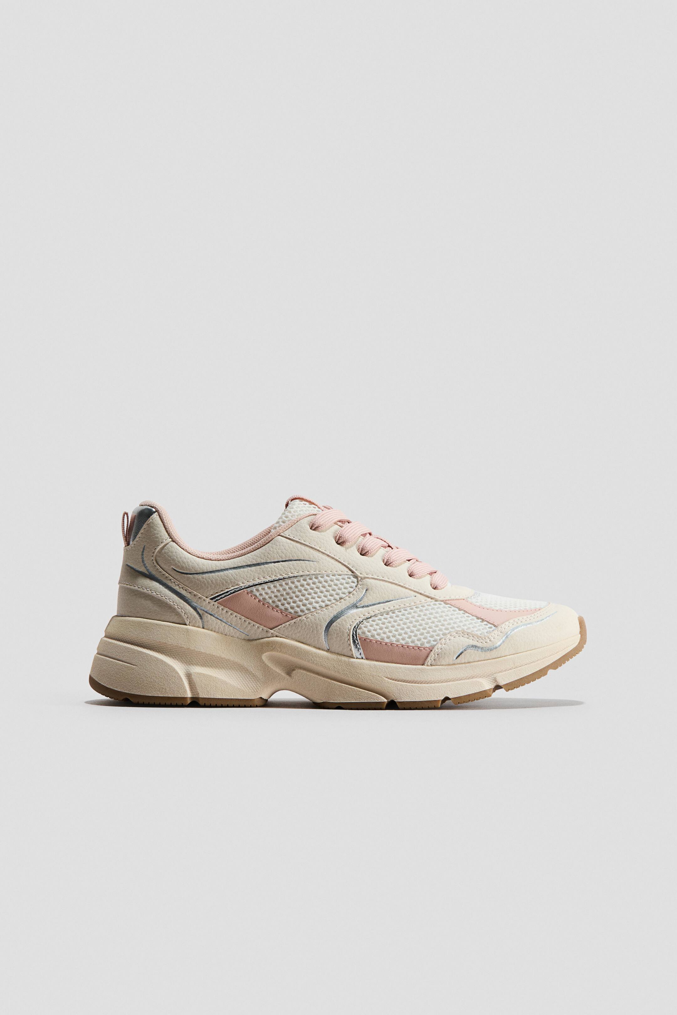 Größeres Bild ansehen: Ein Sneaker wird in einer Seitenansicht präsentiert, mit einem beige-rosa Farbschema, weißen Mesh-Einsätzen und beigen synthetischen Überzügen im Obermaterial. Hellrosa Schnürsenkel fädeln sich durch Ösen, und silberfarbene Akzente zieren die Seitenpaneele, die alle auf einer klobigen beigen Zwischensohle und einer braunen Gummiaußensohle ruhen.