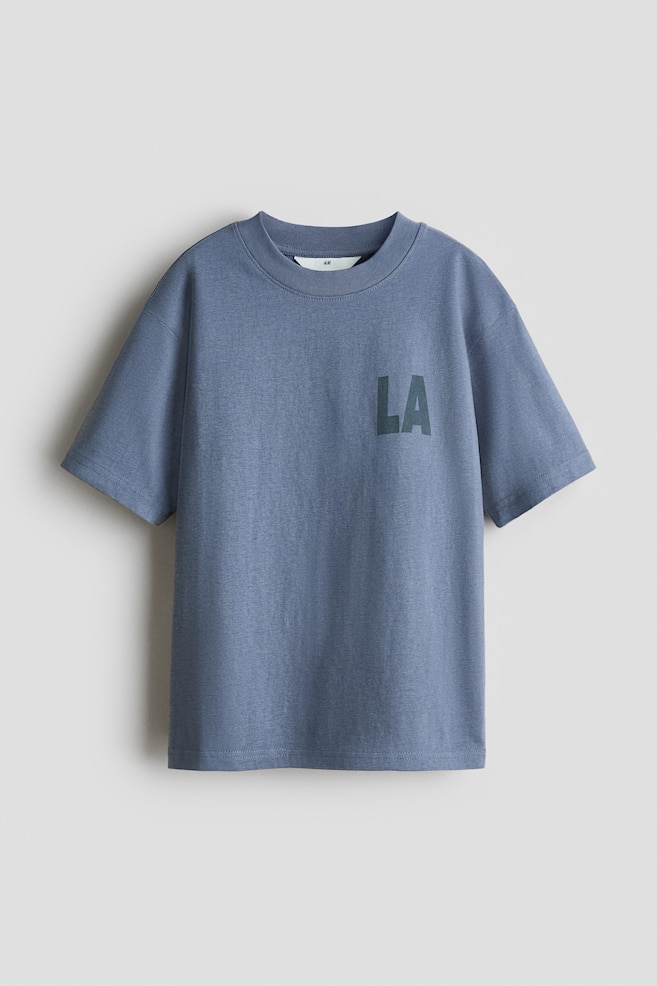 Een losvallend T-shirt in stoffige blauwe bedrukte katoenen jersey, aan de voorkant gericht, met een geribbelde rand rond de halslijn, verlaagde schouders en een donker "LA"-print op het linkerborstgebied. - 1