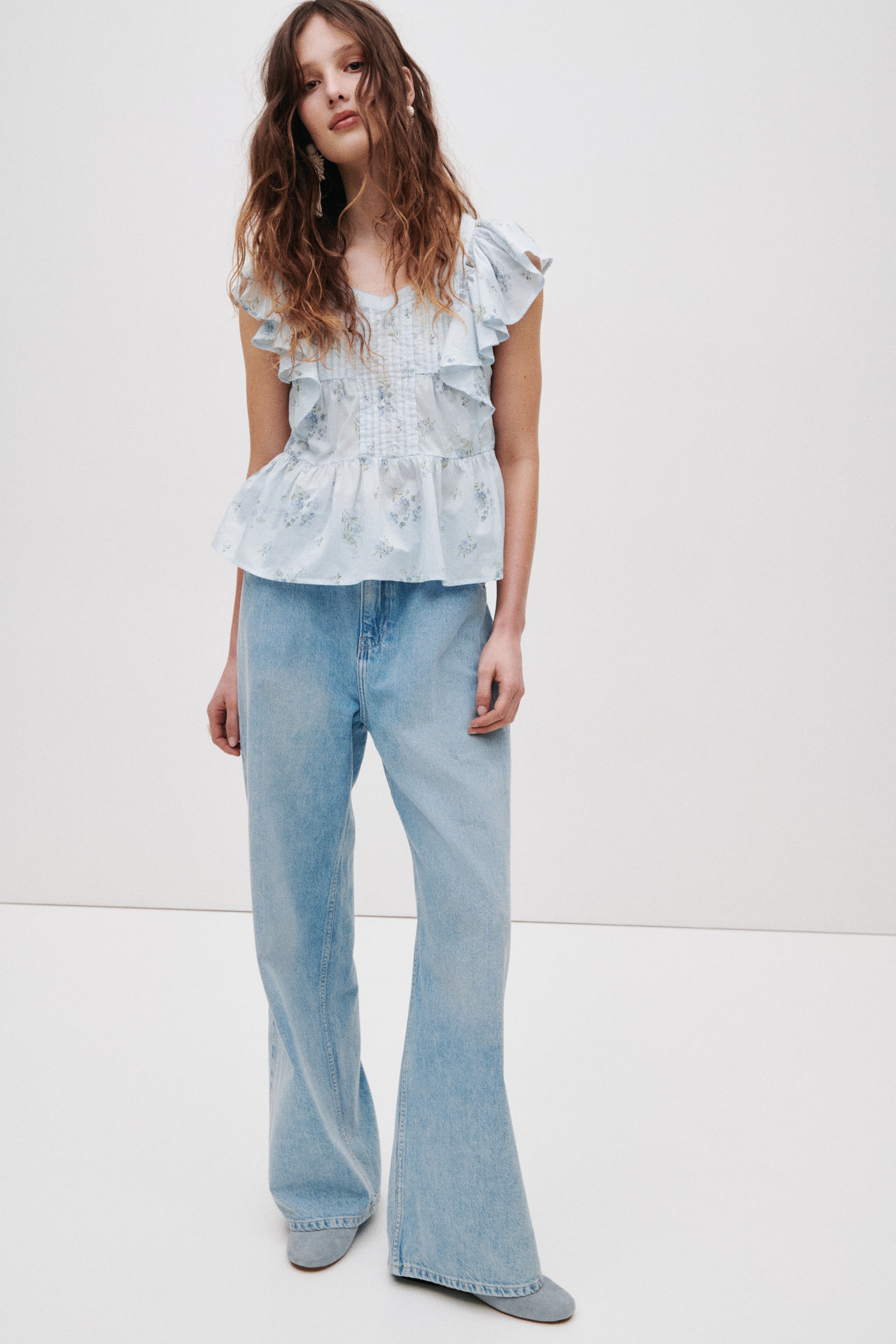 View larger image: A light blue floral peplum top features ruffled cap sleeves, a ruffled V-neckline, and pintucks on the bodice, facing front.