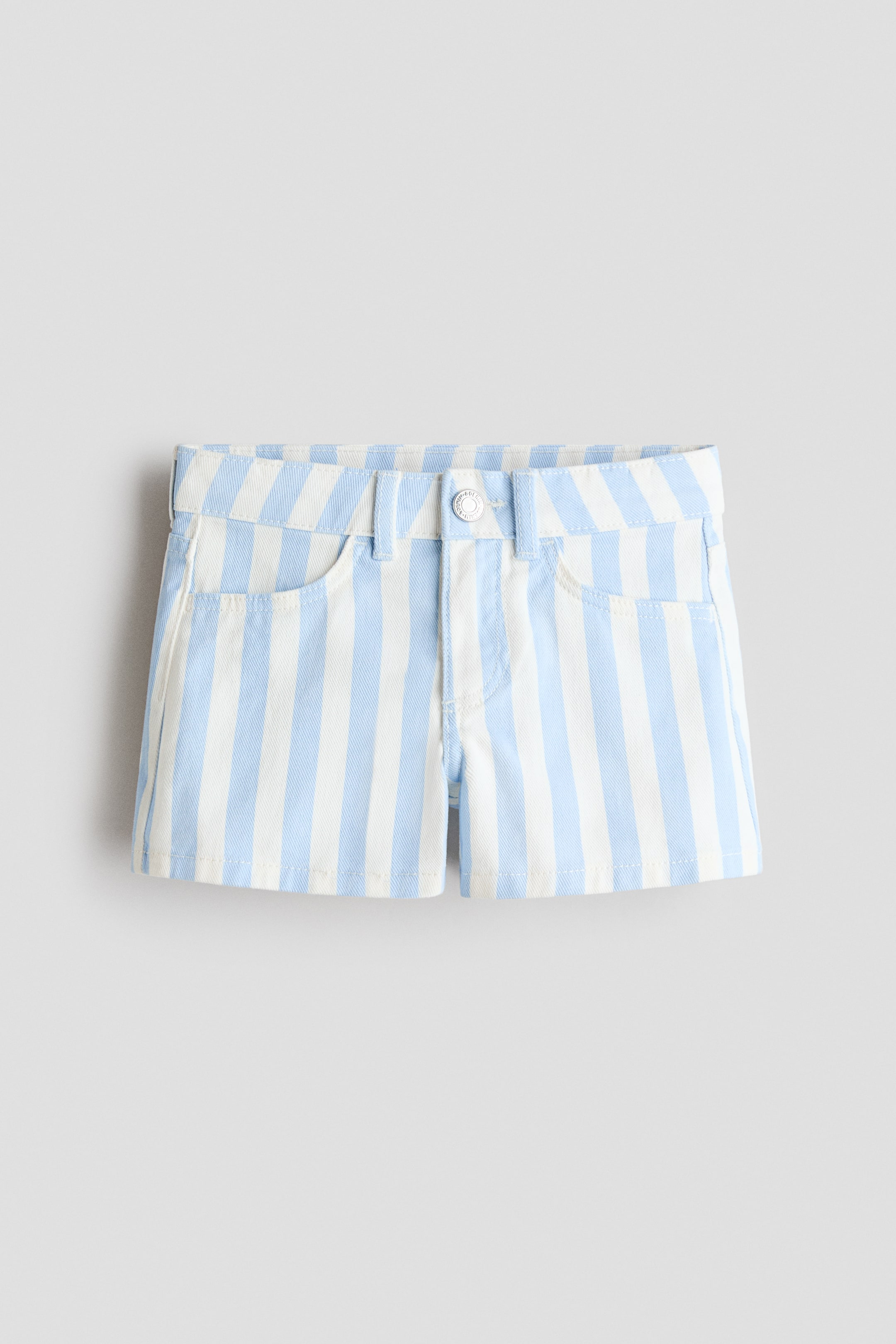 Ingrandisci l'immagine: I pantaloncini sono presentati in vista frontale, caratterizzati da strisce verticali azzurro chiaro e bianche su denim di cotone. La vita mostra passanti per cintura e un bottone color argento che chiude una patta con cerniera, posizionata sopra due tasche anteriori stilizzate.