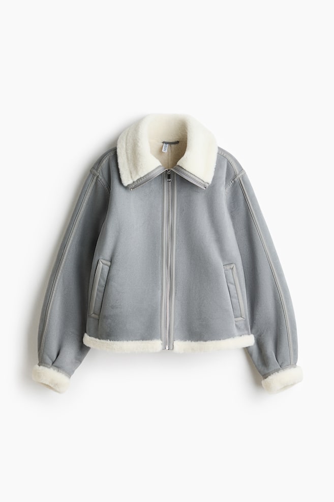 A grey cropped jacket is shown front-on, featuring a wide white faux shearling collar, cuffs and hem. A full-length zip runs down the front, and side welt pockets are visible. - 1