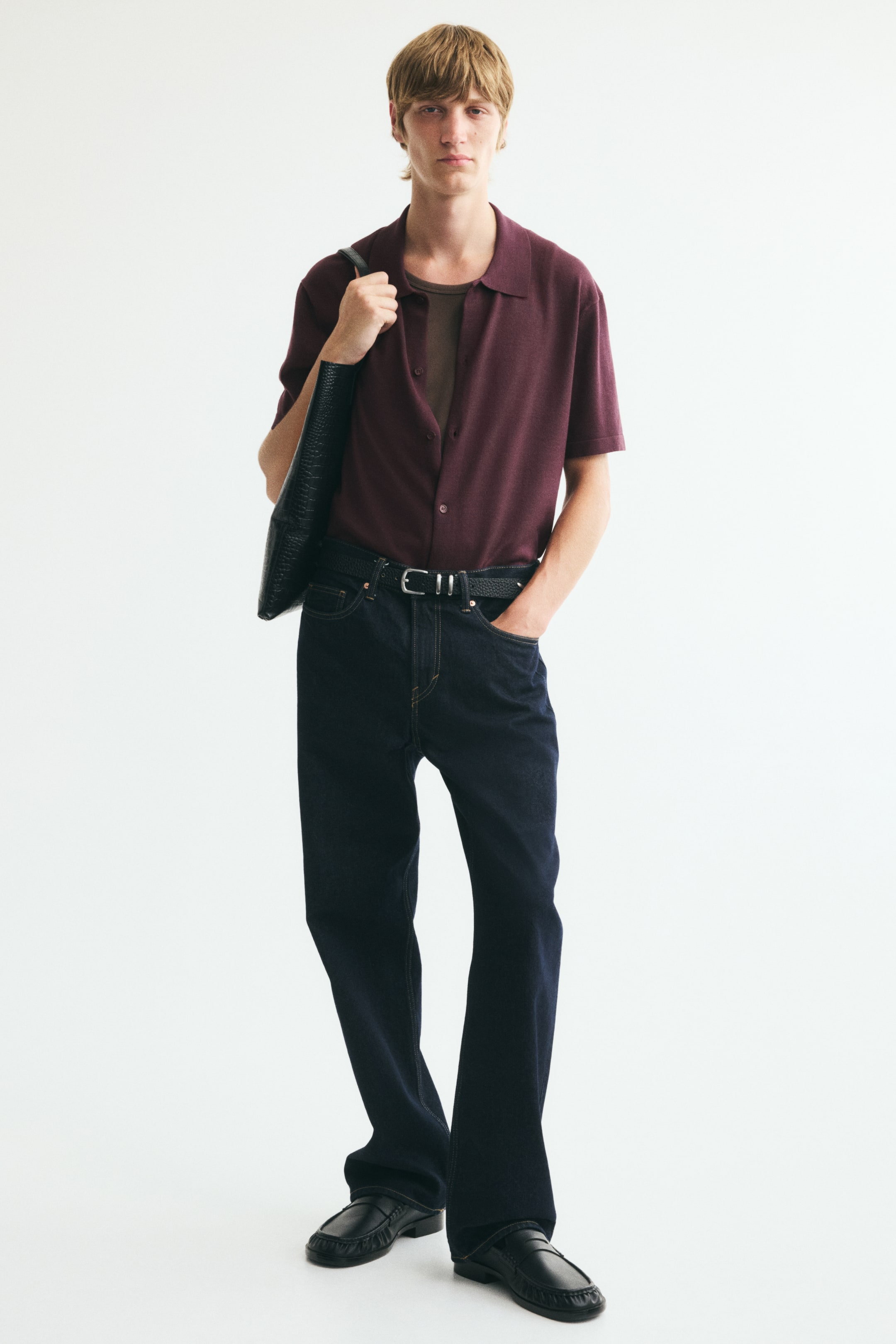 View larger image: The model is wearing a burgundy short-sleeve knit shirt, styled open over a brown T-shirt and tucked into dark jeans. The shirt features a classic collar, a buttoned French front, and a relaxed, regular fit.