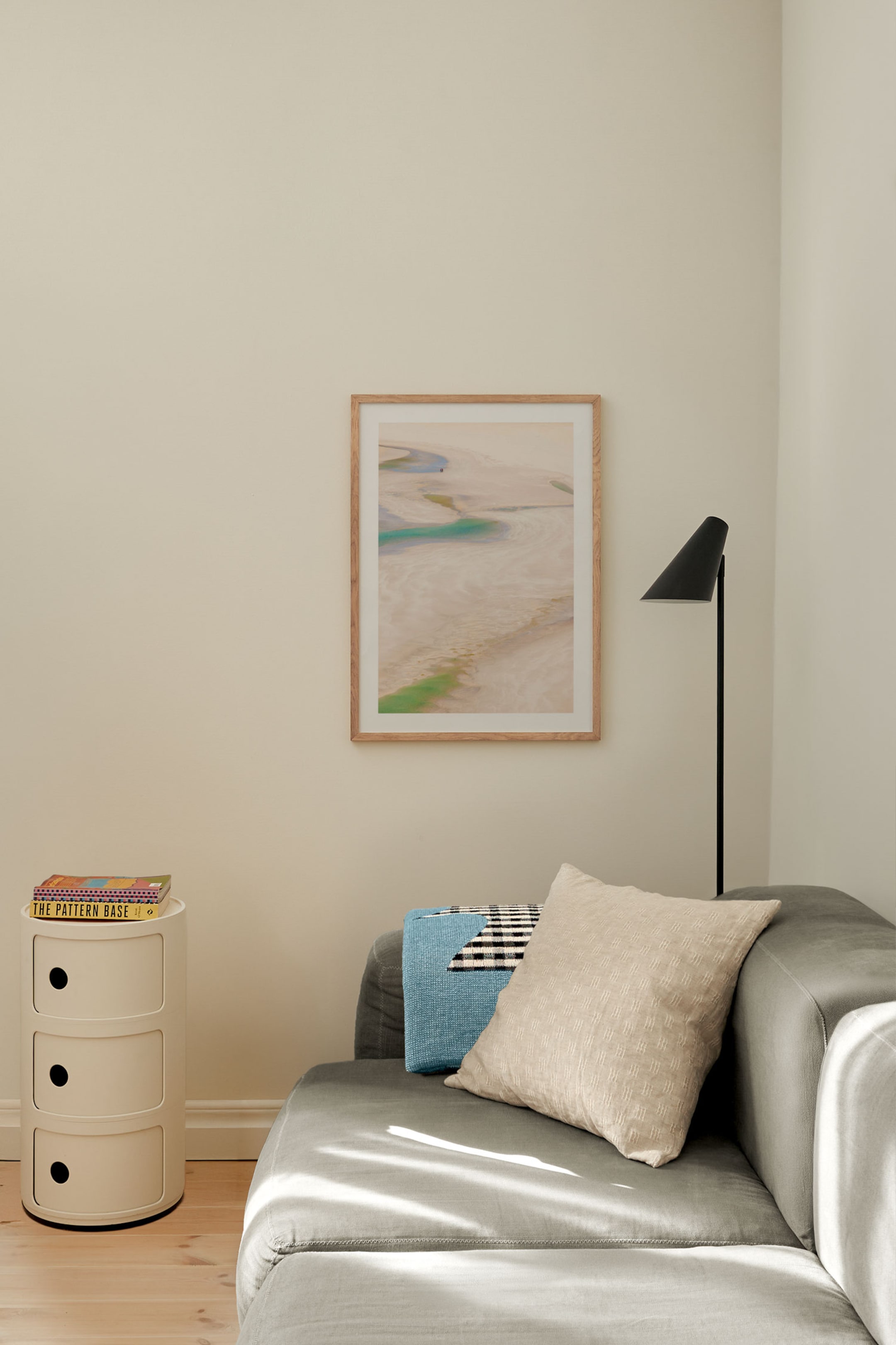 Visualizza immagine più grande: Un'opera d'arte incorniciata in verticale presenta un paesaggio aereo astratto con forme nei toni del beige sabbia, azzurro chiaro e verde, presentata in una cornice di legno chiaro con passepartout bianco.