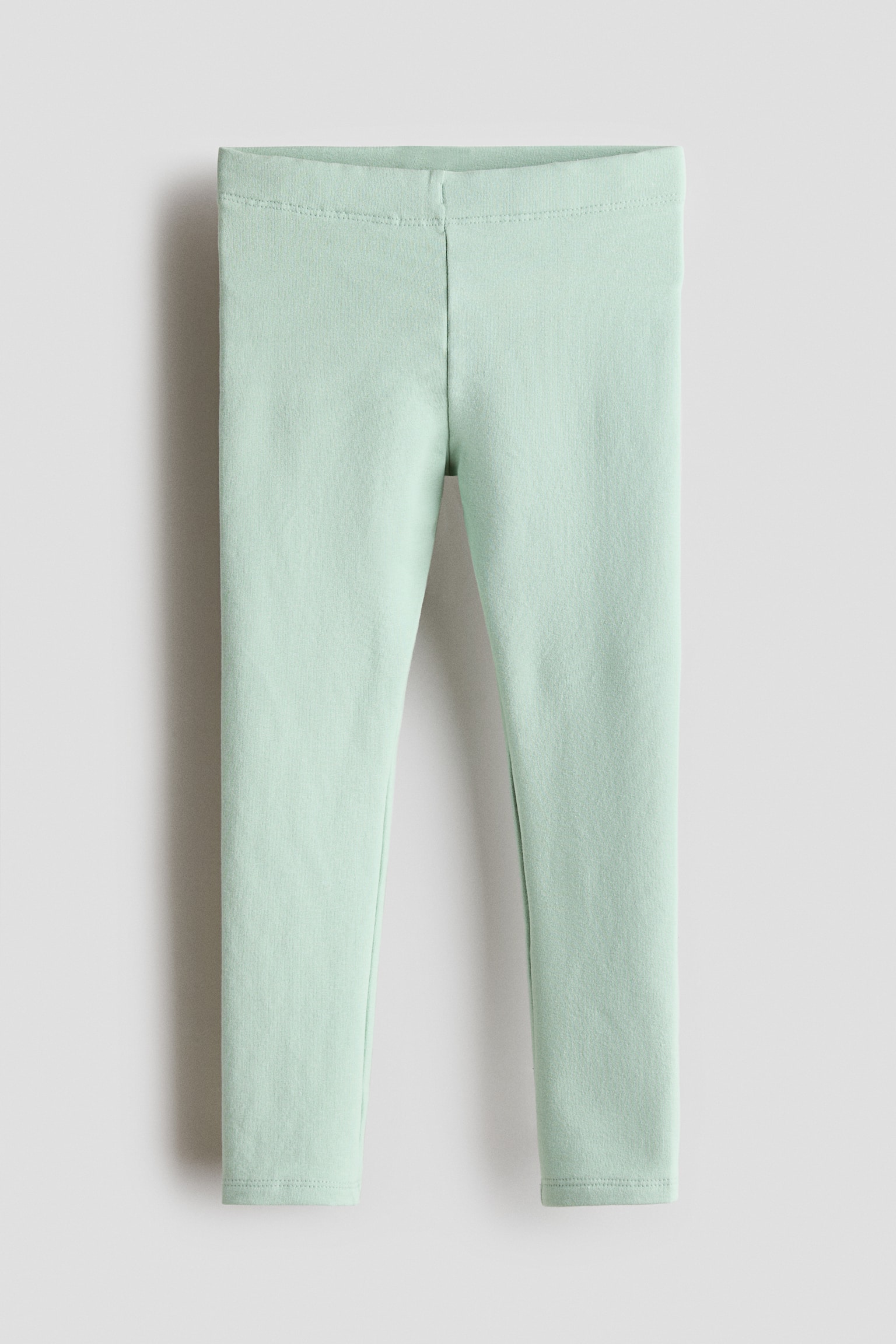 Mint green leggings are shown from the front, featuring a wide elasticated waistband and slim-fitting legs. The leggings are displayed flat, highlighting their clean seams and ankle-length hems.