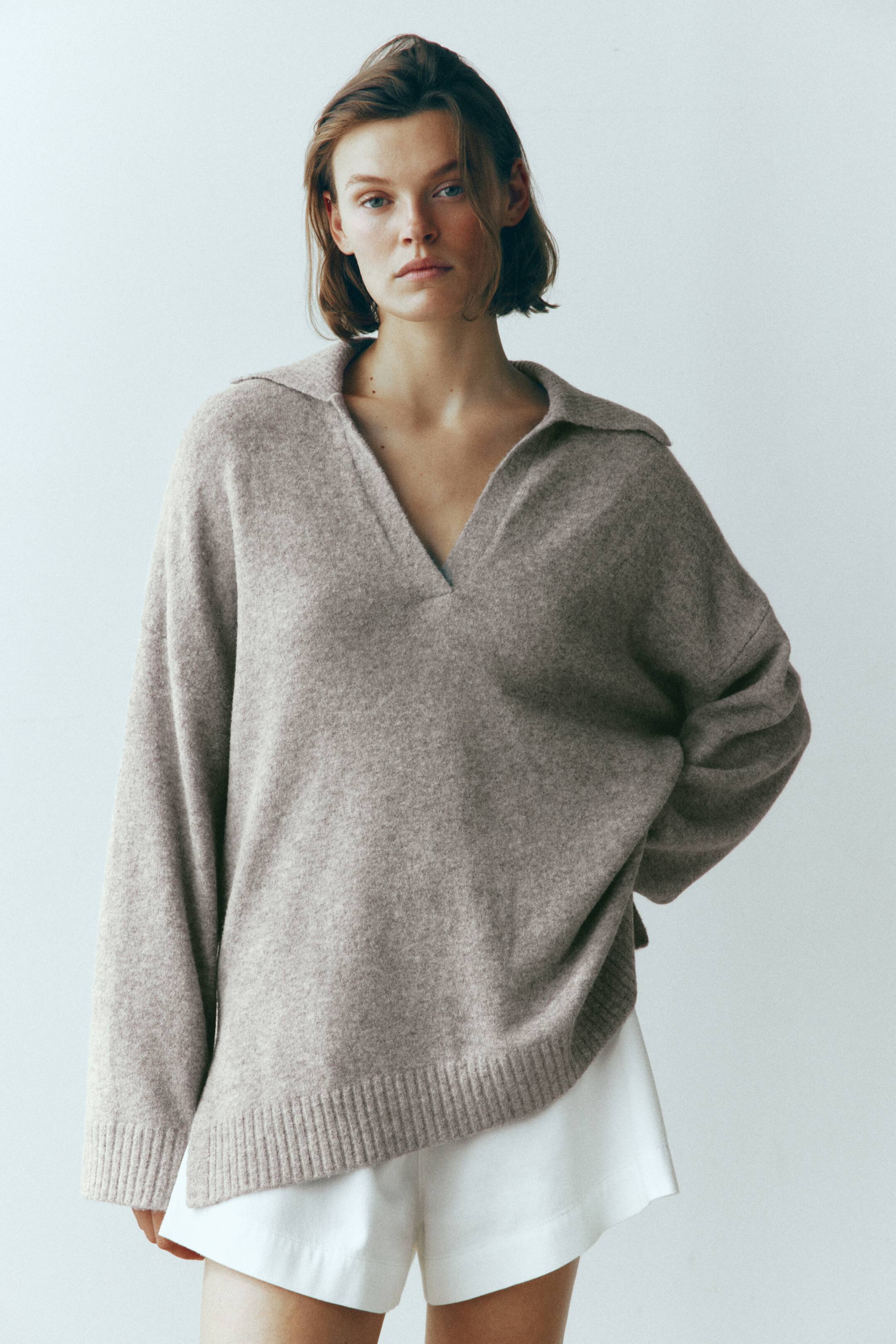 View larger image: A loose-fit, taupe knit sweater is being worn by the model, featuring a collar with a V-shaped neckline, dropped shoulders, and ribbed cuffs. The sweater has a relaxed drape and is paired with white shorts, highlighting its ribbed hem.