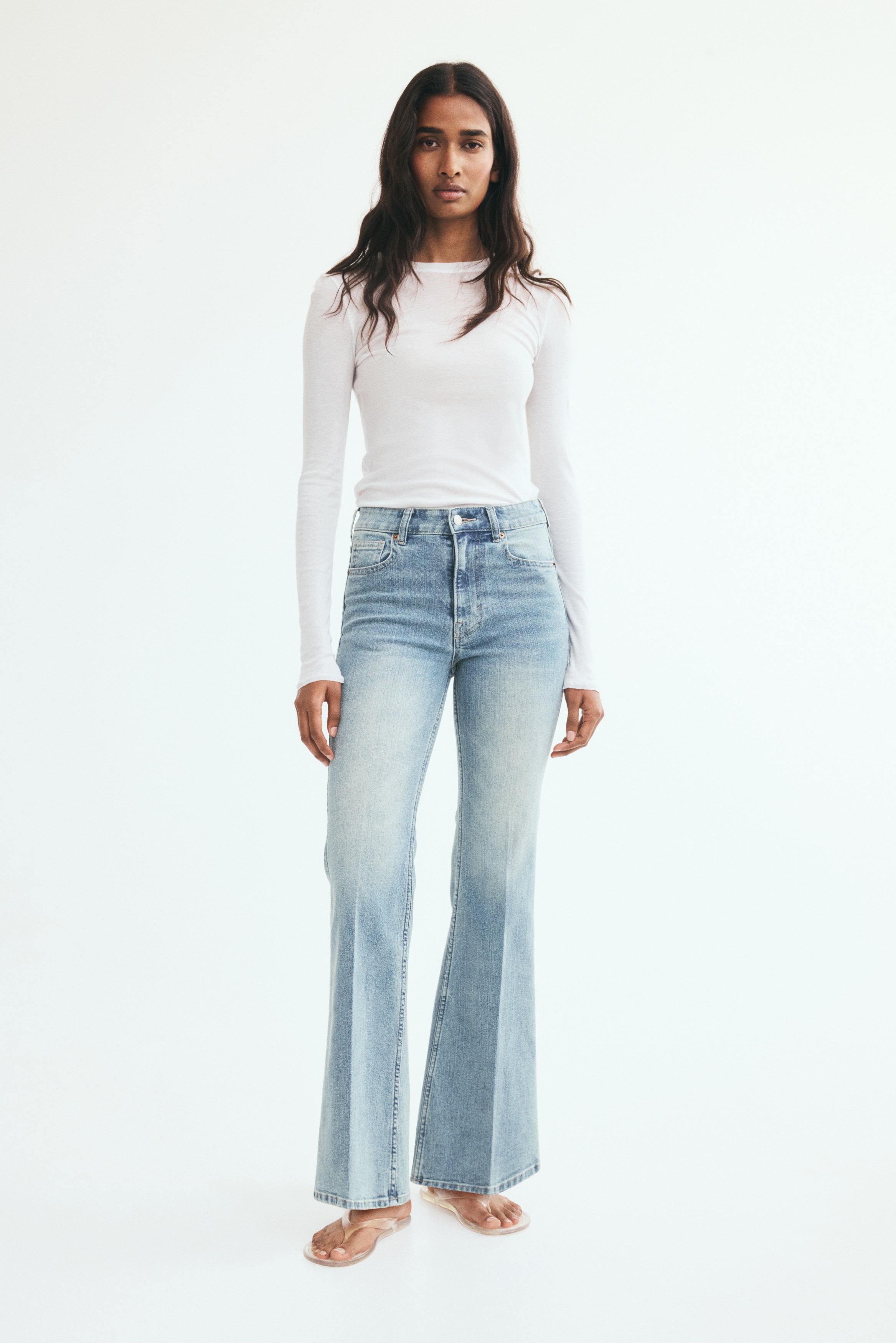 Light blue flared jeans feature a faded wash with lighter distressed areas on the thighs, showcasing a front button fly closure, belt loops, and two front pockets with rivets.