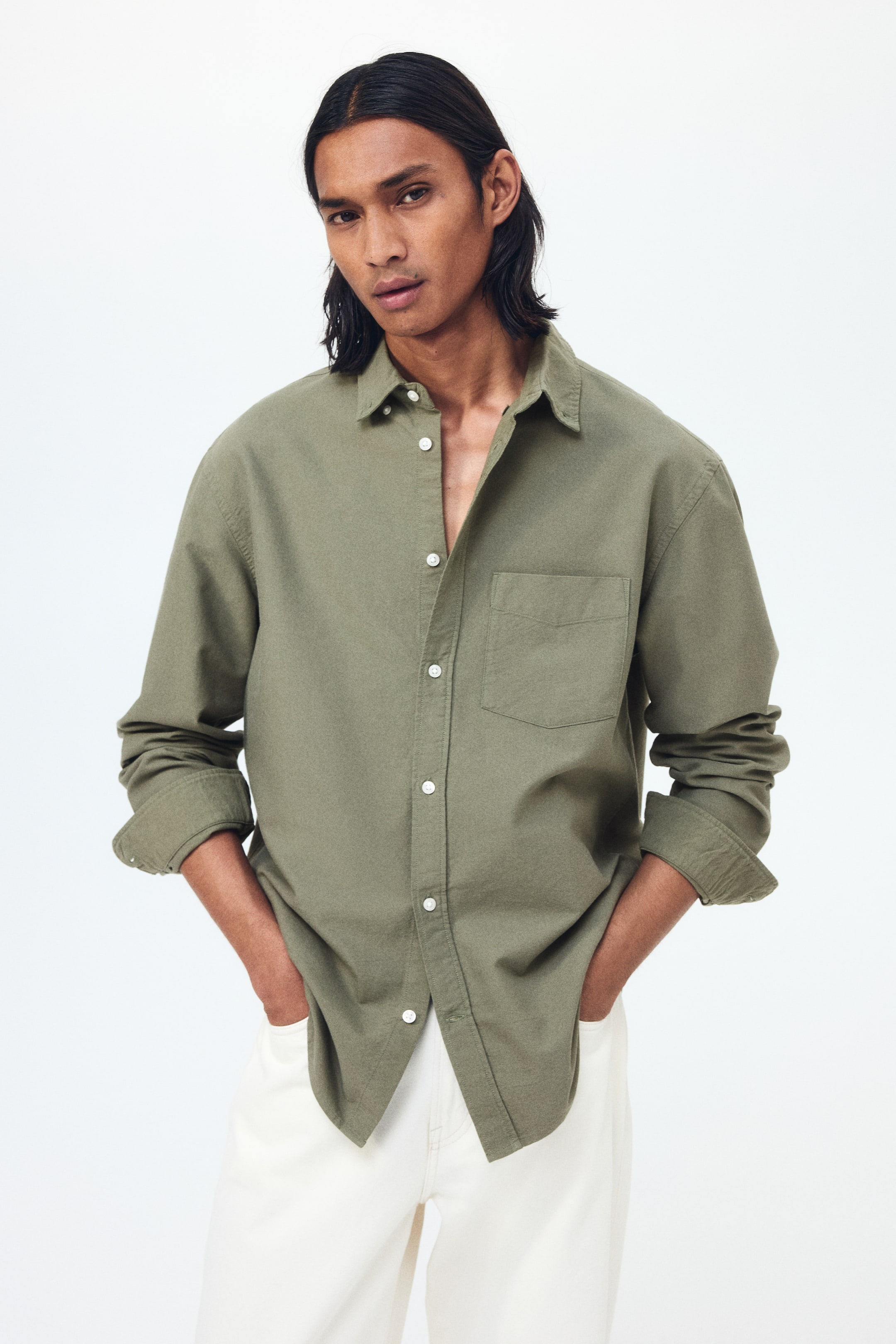 View larger image: An olive green long-sleeved shirt featuring a spread collar, white buttons down the front with the top few open, and a single patch pocket on the left chest. Its long sleeves are rolled up to the forearms, offering a relaxed fit.