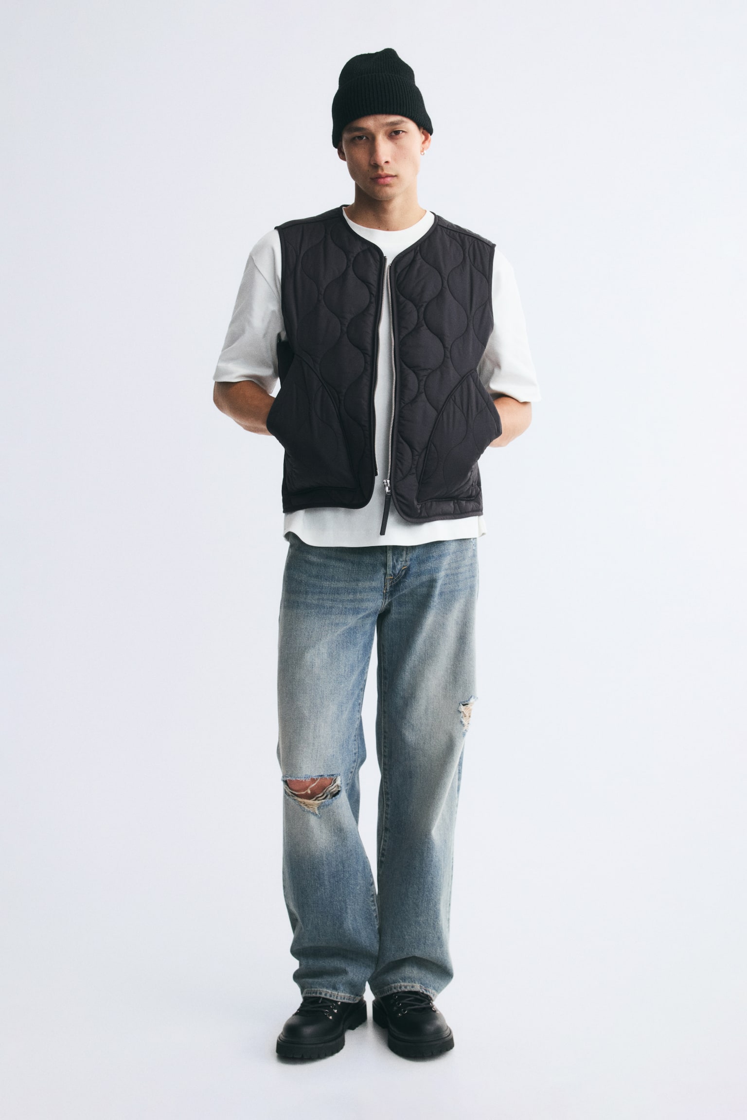 A black quilted nylon gilet with a round neckline and front zip is being worn by the model over a white T-shirt. The model has their hands in the giletâs front patch pockets. - 1