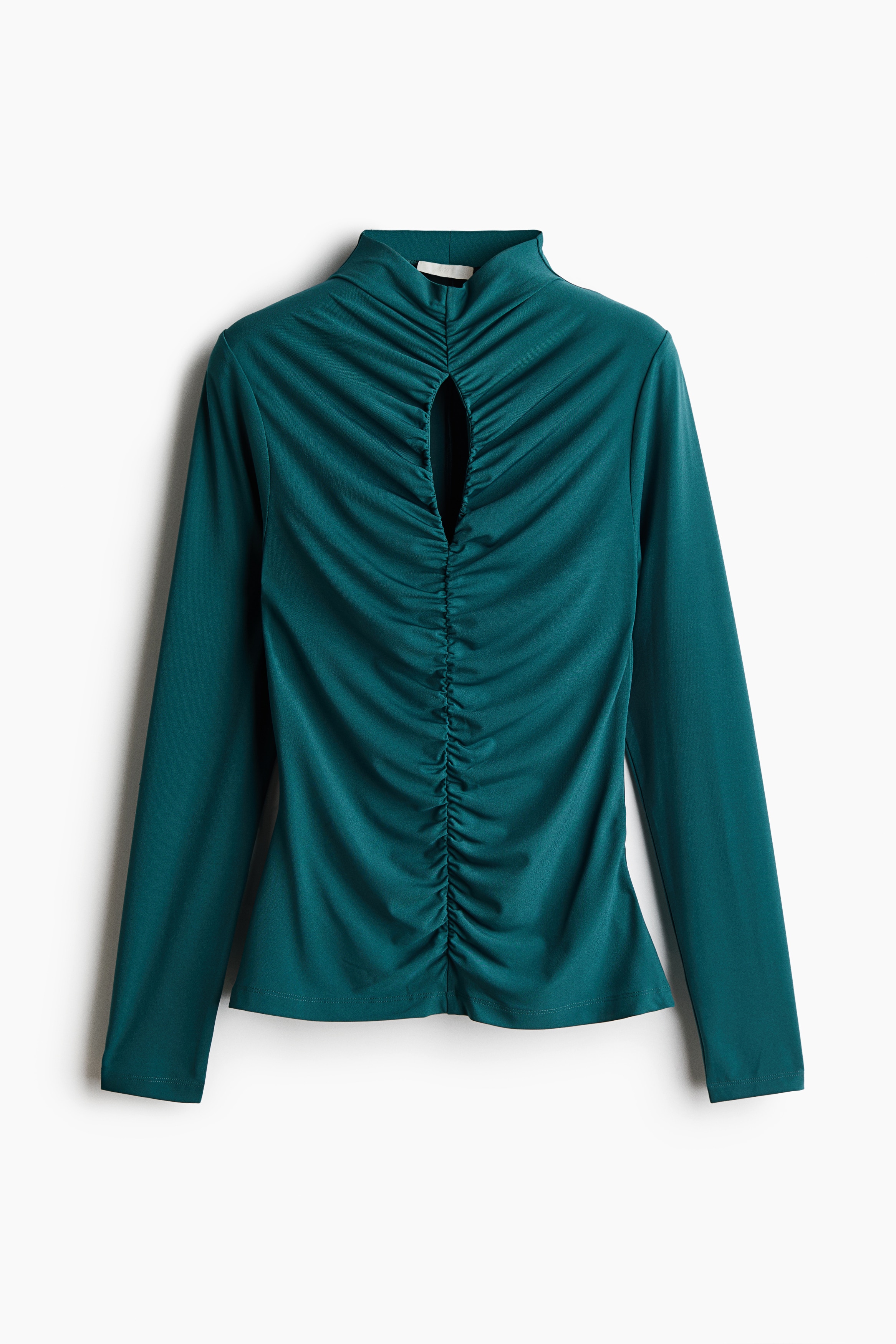 A dark teal, fitted stretch jersey top featuring a high neck, a front keyhole cut-out, and central gathering for a draped effect is being worn by the model. The long-sleeved top is styled with black wide-leg trousers and a black leather jacket draped around the arms.