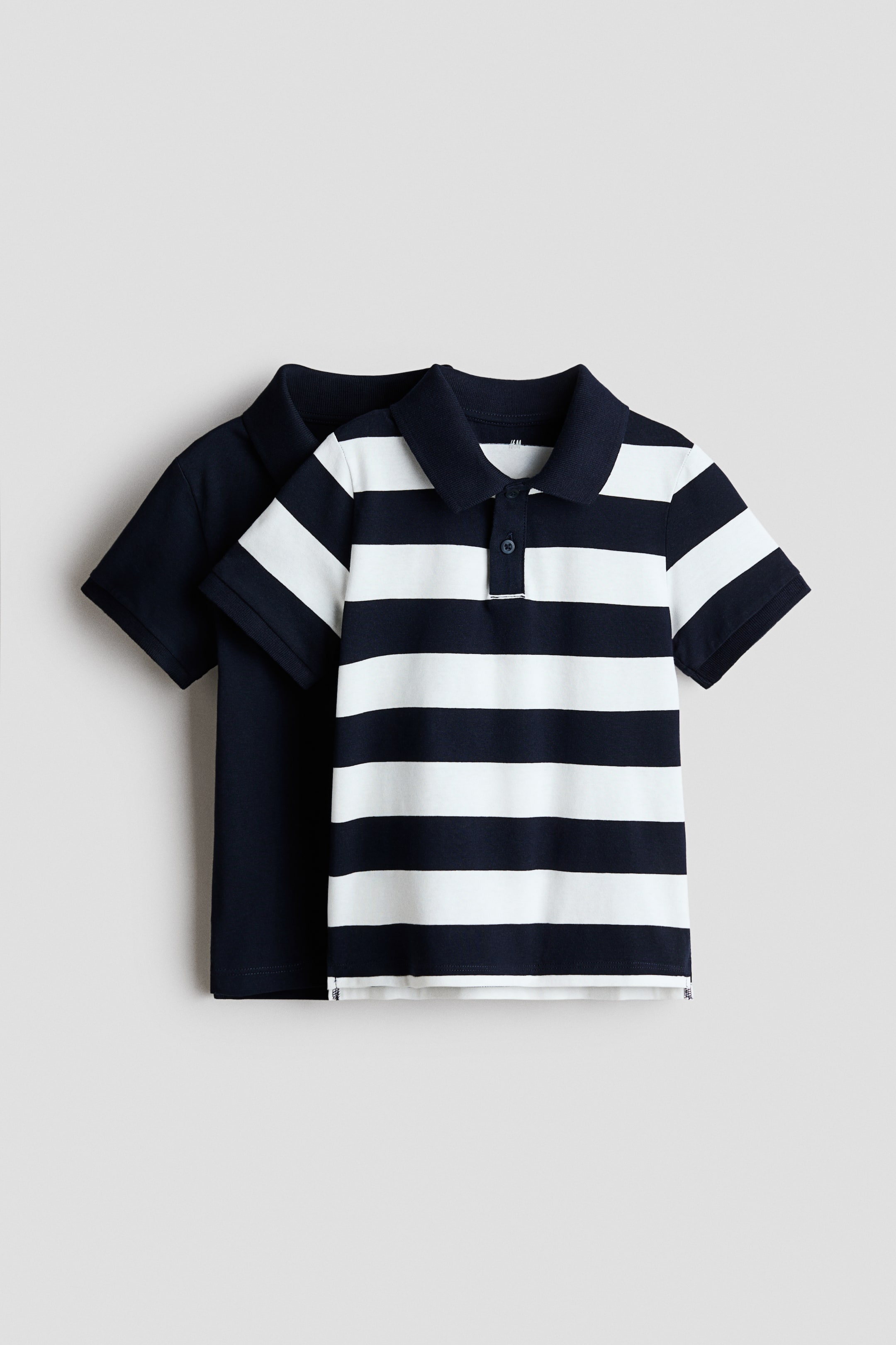 View larger image: Two polo shirts are offered as a set, with a navy blue and white striped polo shirt prominently displayed in the FRONT. This striped shirt boasts a classic collar and a two-button placket, while a solid navy blue polo shirt is elegantly layered behind it.