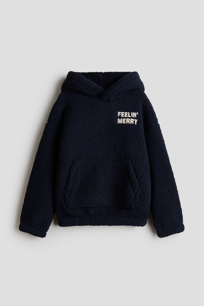 Ein navyblauer Oversize-Teddy-Fleece-Hoodie ist von vorne zu sehen und verfÃ¼gt Ã¼ber eine Wickelkapuze, Ã¼berschnittene Schultern und eine vordere KÃ¤ngurutasche. Auf der linken Brust ist eine cremefarbene gestickte Aufschrift mit dem Text âFEELIN' MERRYâ zu sehen. - 1