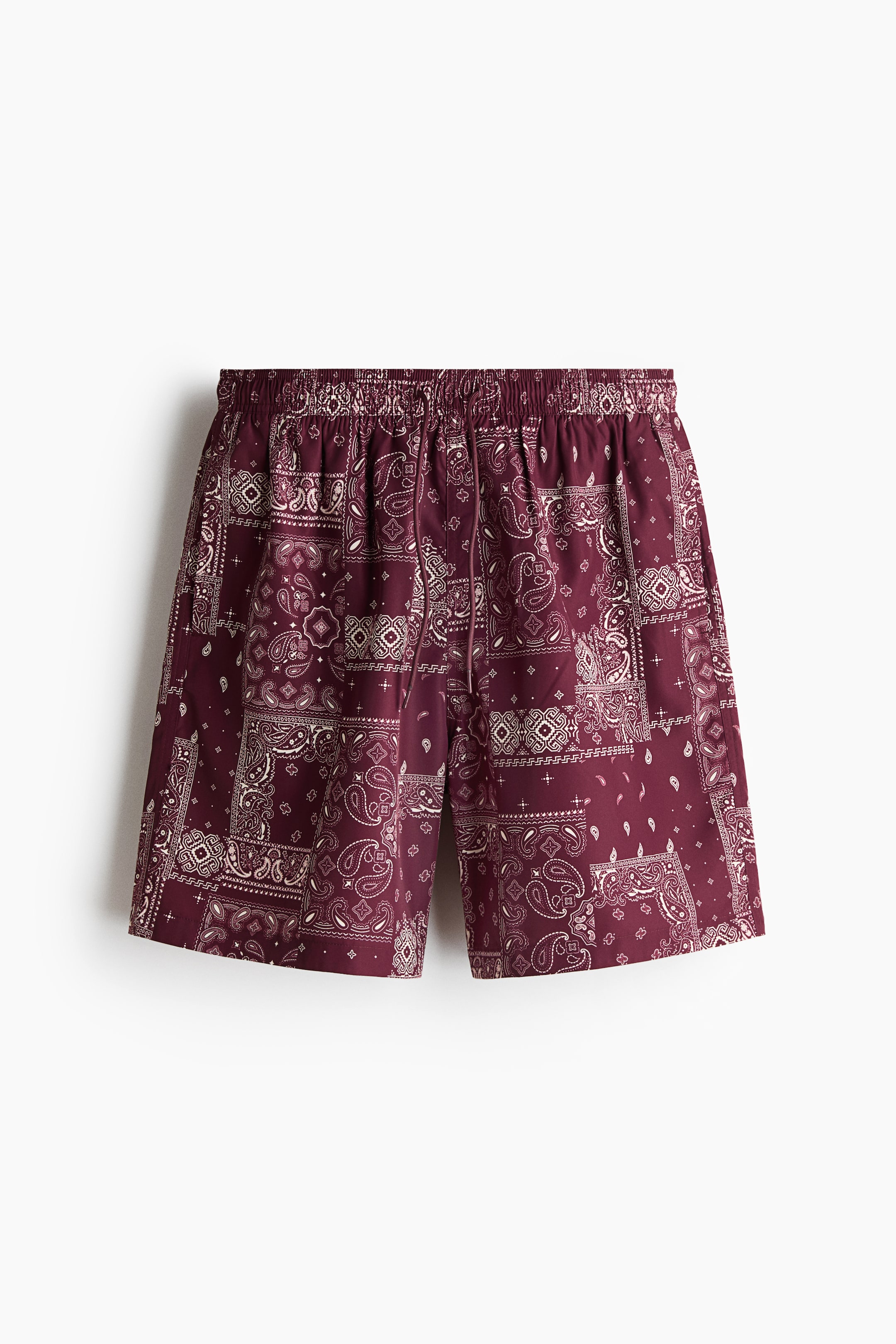 View larger image: Maroon swim trunks featuring a white bandana print on woven fabric are displayed from the front. They're designed with a covered elastic waistband, a visible drawstring, and subtly outlined side pockets.