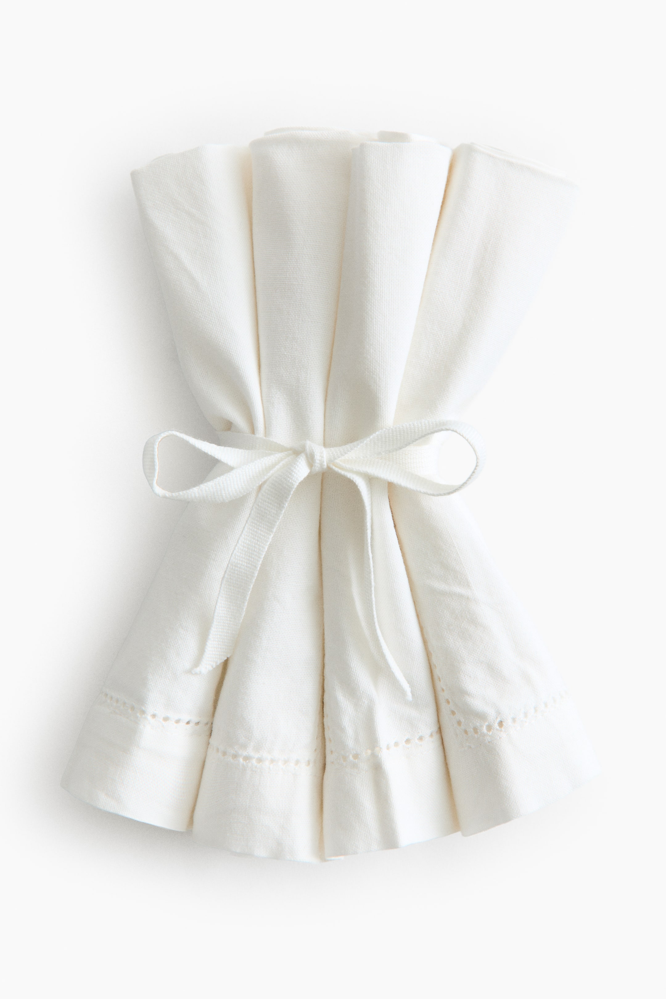View larger image: Napkins in cotton canvas are folded and bundled into a fan-like arrangement, secured at the centre with a matching ribbon. The visible edges show a 2.5 cm hem with hemstitch detailing.