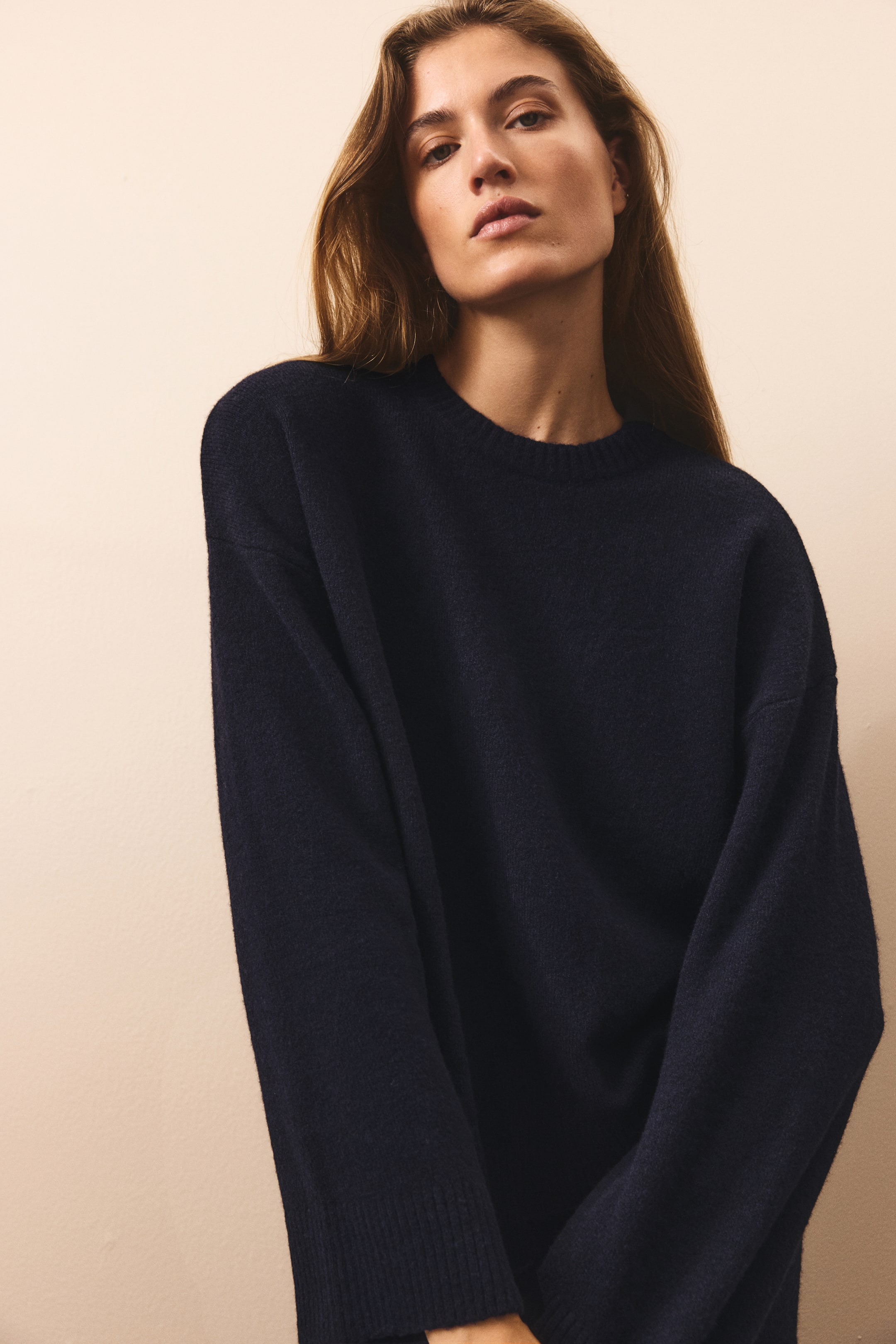 View larger image: A dark navy knit sweater is shown from the front, featuring a round, rib-trimmed neckline, dropped shoulders, and long, relaxed sleeves with ribbed cuffs. The garment shows a soft, textured knit surface and a loose, comfortable fit.