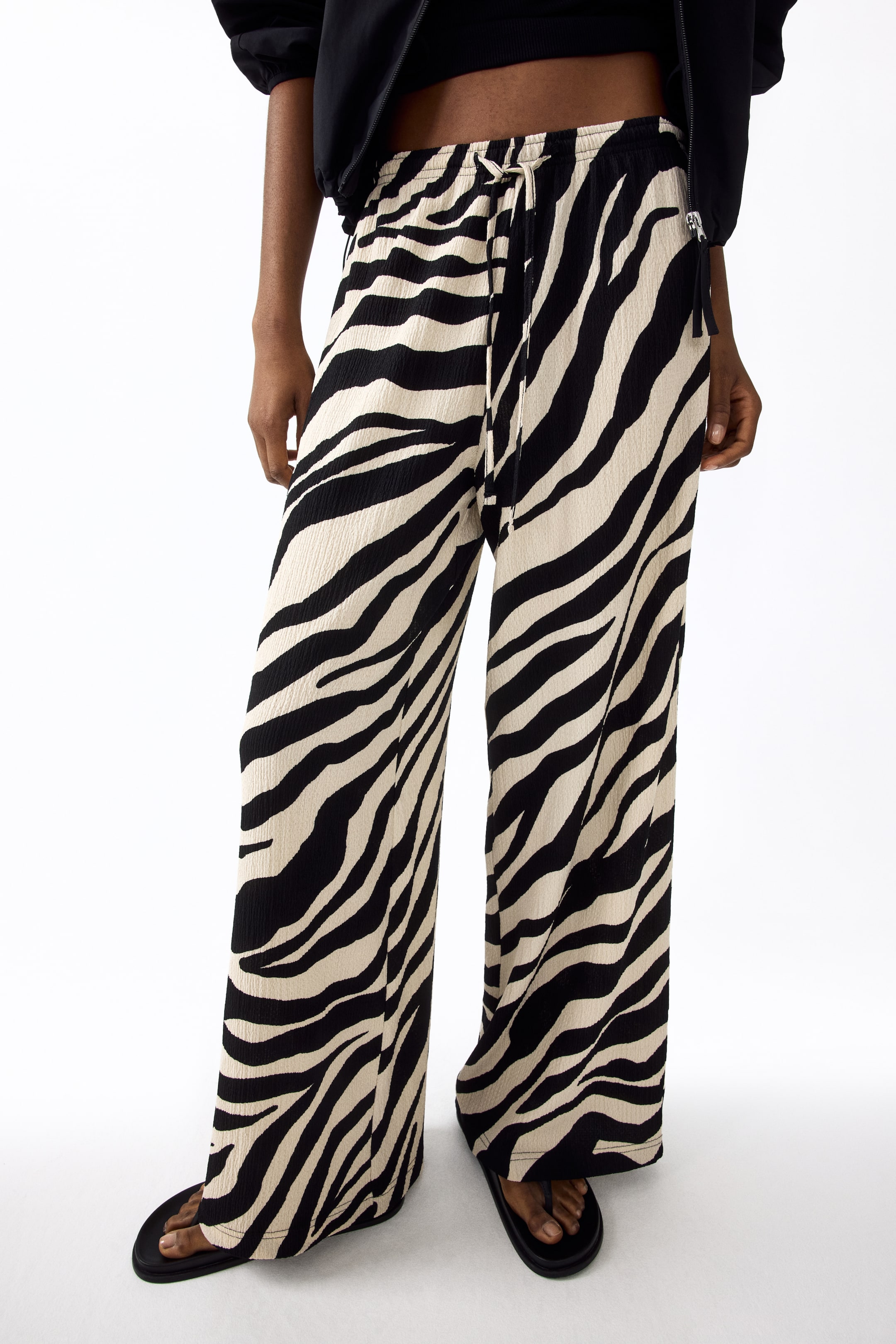 View larger image: Loose-fit trousers in black and beige zebra print jersey are being worn by the model, featuring a high, elasticated, drawstring waist with the drawstring tied, and wide legs.
