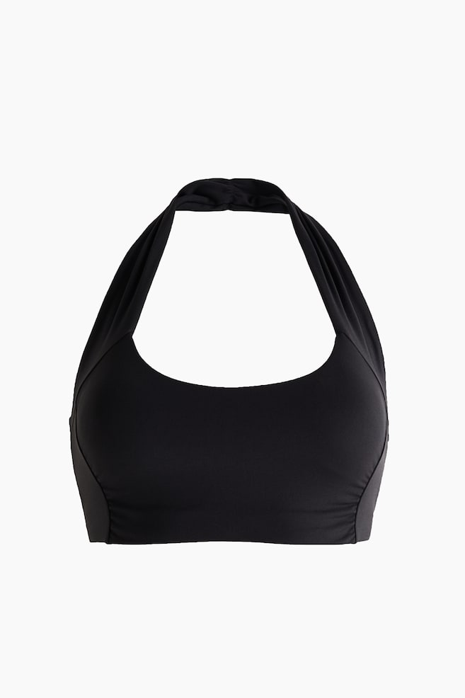 A black halter-neck top is shown from the front, featuring a scoop neckline and wide, gathered straps that loop behind the neck. The top showcases a supportive wide underband and structured side panelling for a streamlined fit. - 1
