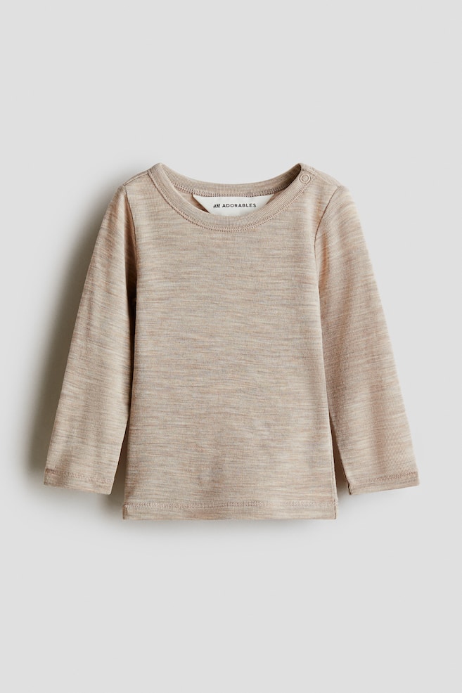 A light beige, long-sleeved top is presented facing front, featuring a round neckline with ribbed trim and a single snap button on the left shoulder. It is displaying ribbed cuffs, small side slits at the hem, and a marled knit texture. - 1