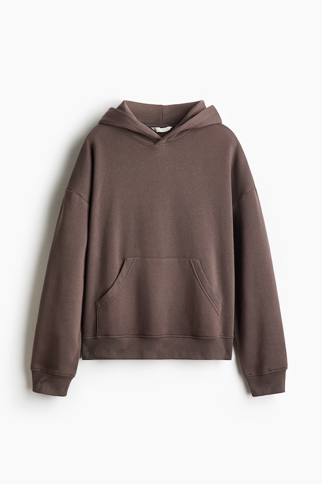 A dark brown sweat fabric hoodie is facing the front, showcasing a double-layer hood, low dropped shoulders, and a front kangaroo pocket. The garment is displaying ribbed cuffs and a matching ribbed hem. - 1
