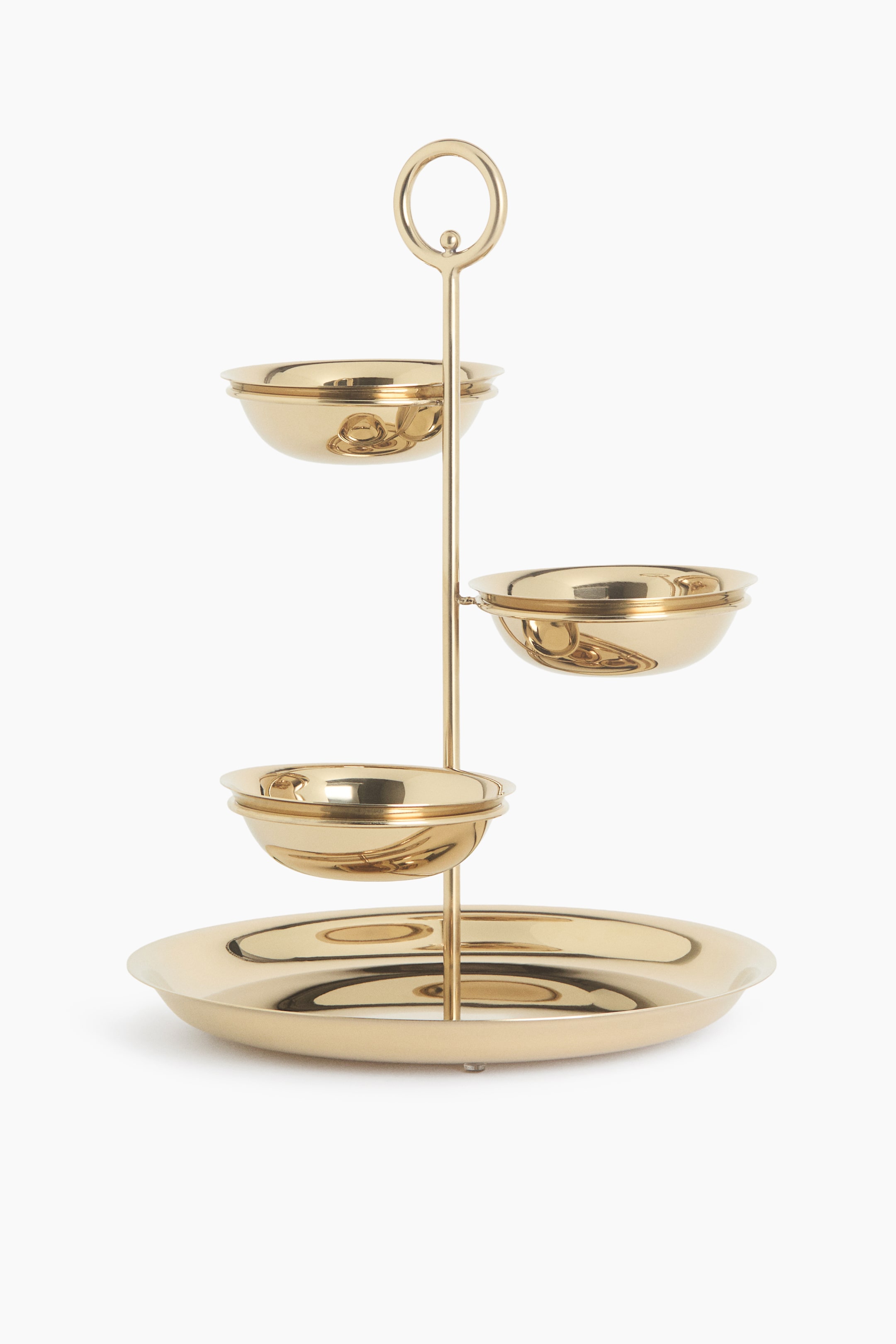 View larger image: A gold-toned tiered serving stand is shown from the front, featuring a central vertical rod topped with a circular ring handle. The stand supports three small, polished bowls arranged at different heights and angles, all resting on a wide, flat circular base tray.