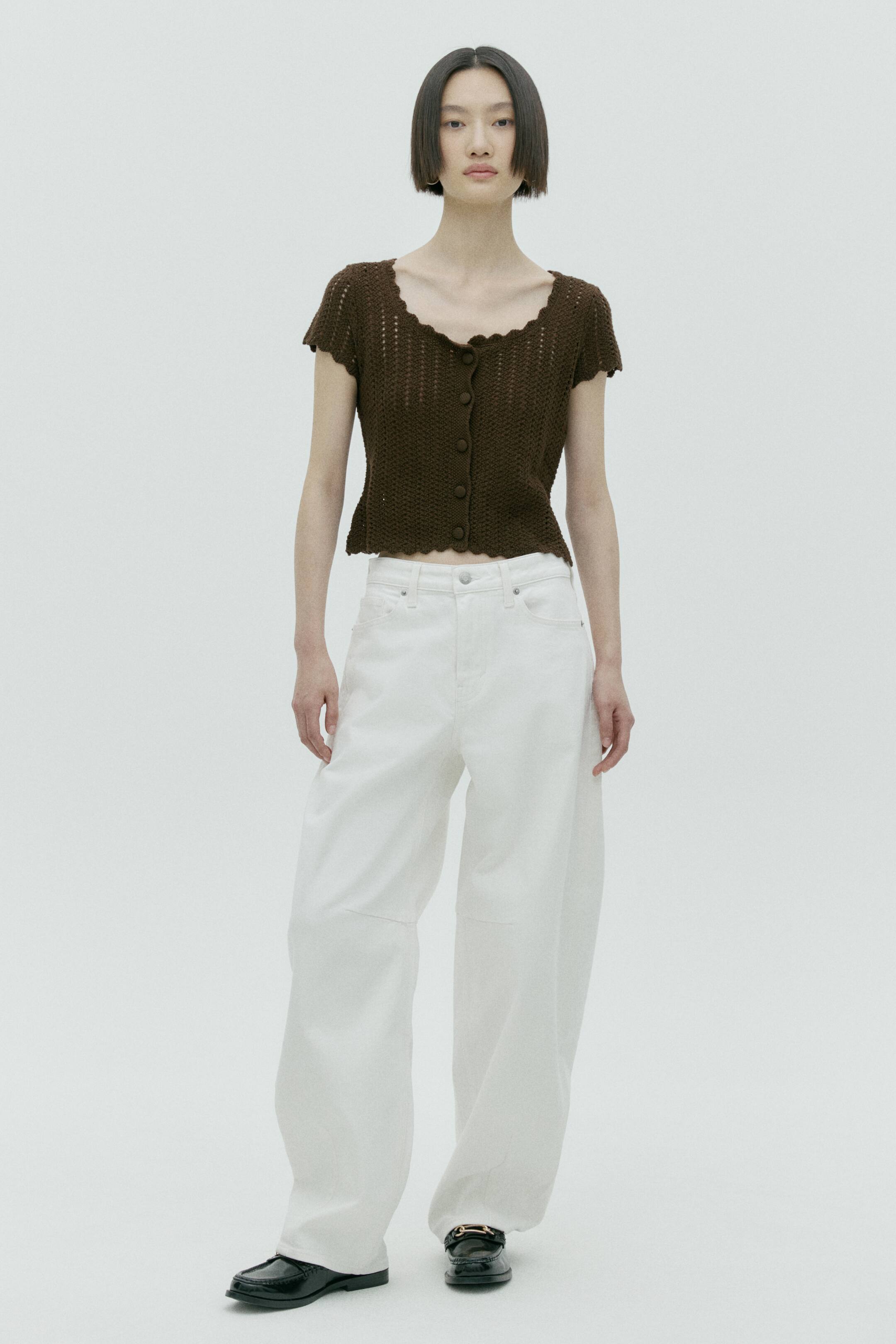 View larger image: A dark brown crocheted short-sleeved top features a scalloped neckline and a matching scalloped hem. It showcases an open-knit pattern and a front button closure with five dark brown buttons.