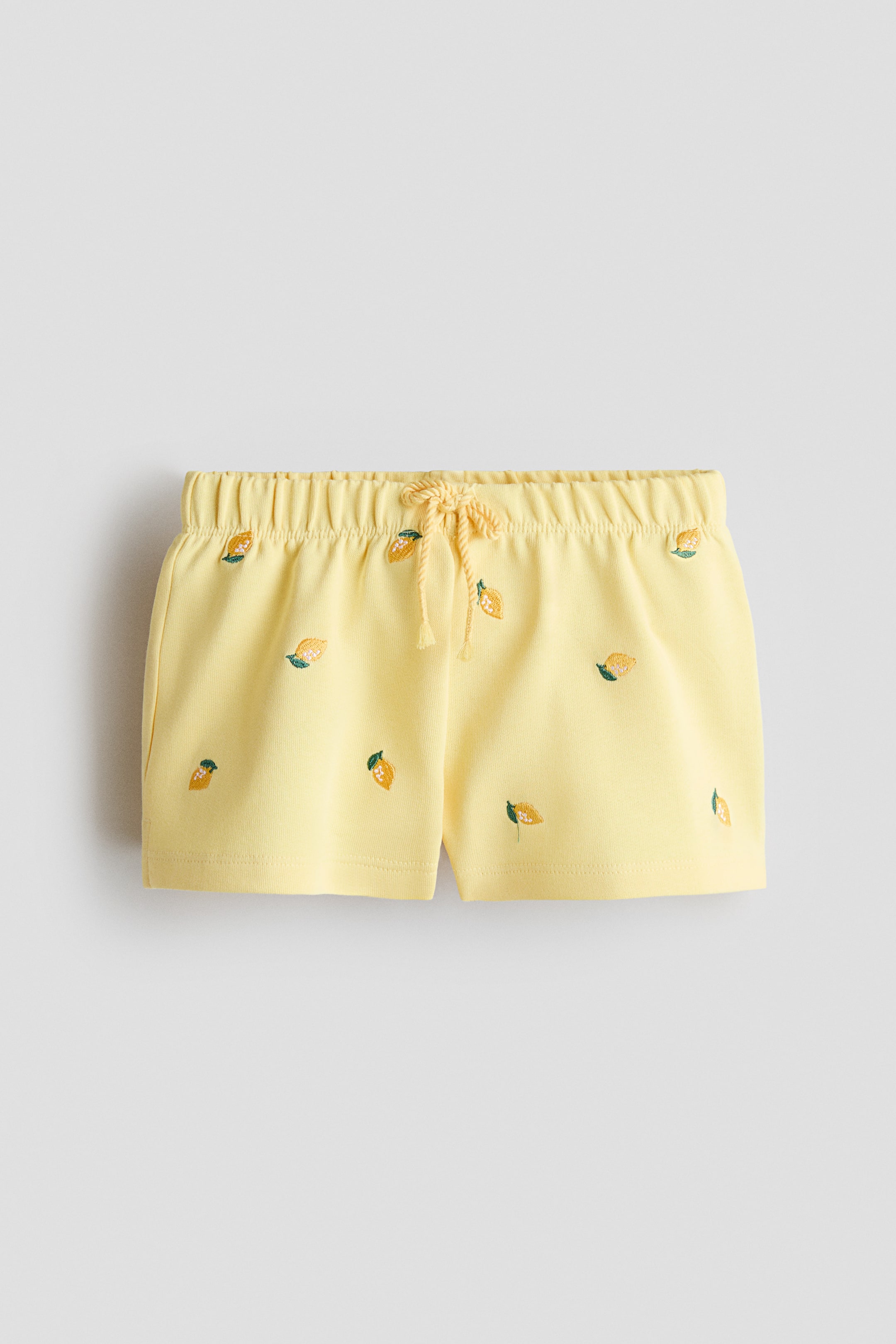 Größeres Bild ansehen: Gelbe Shorts mit einem elastischen Bund und einer vorderen Kordelzugbindung. Die Shorts zeigen gestickte Zitronen-Motive, die über den Stoff verstreut sind, und sichtbare Seitentaschen.