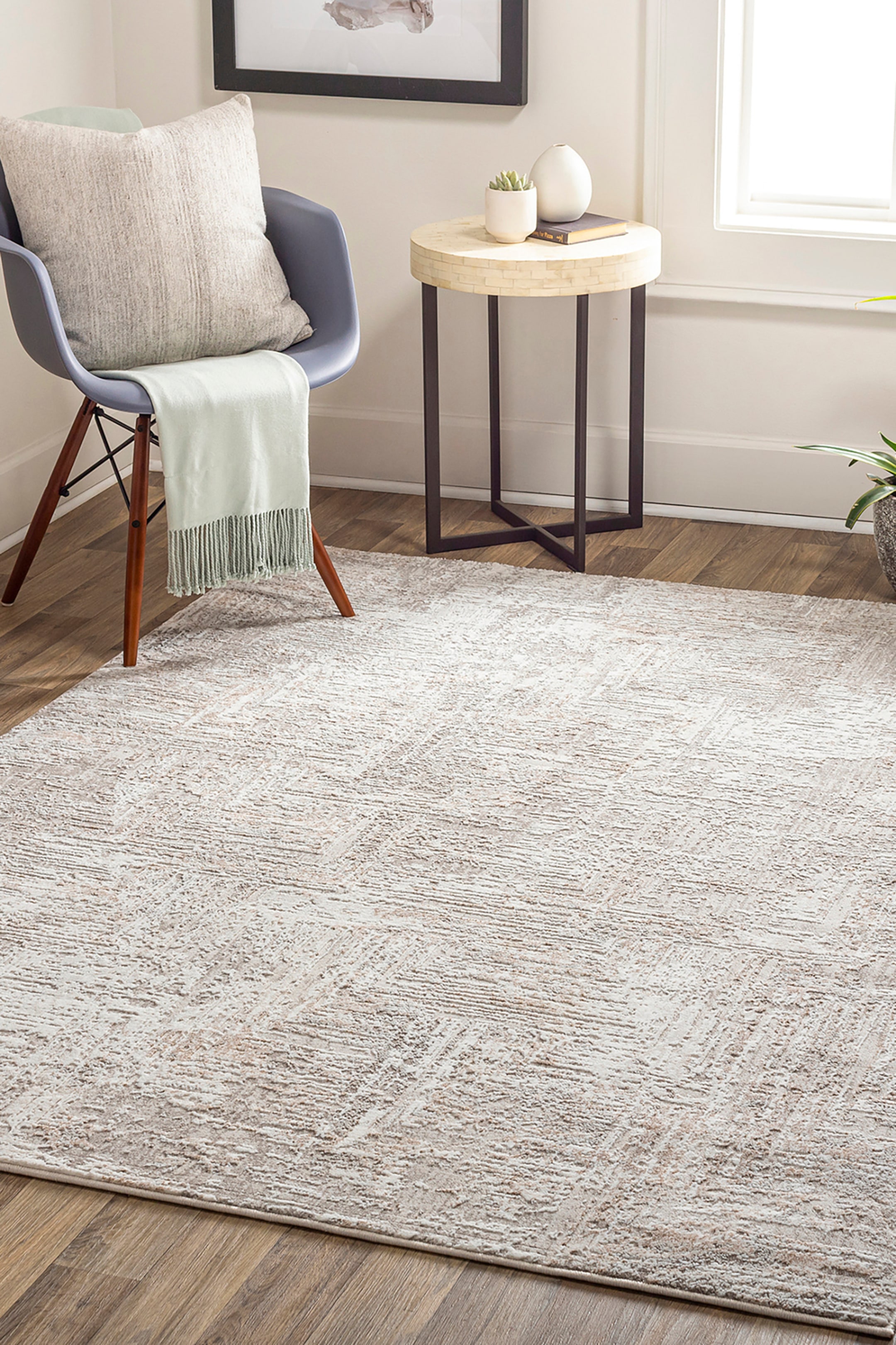 View larger image: A rectangular area rug is lying flat, showcasing a textured, high-low pile with a distressed finish. The rug features an abstract geometric pattern composed of intersecting textured lines in neutral shades of cream, beige, and light grey.