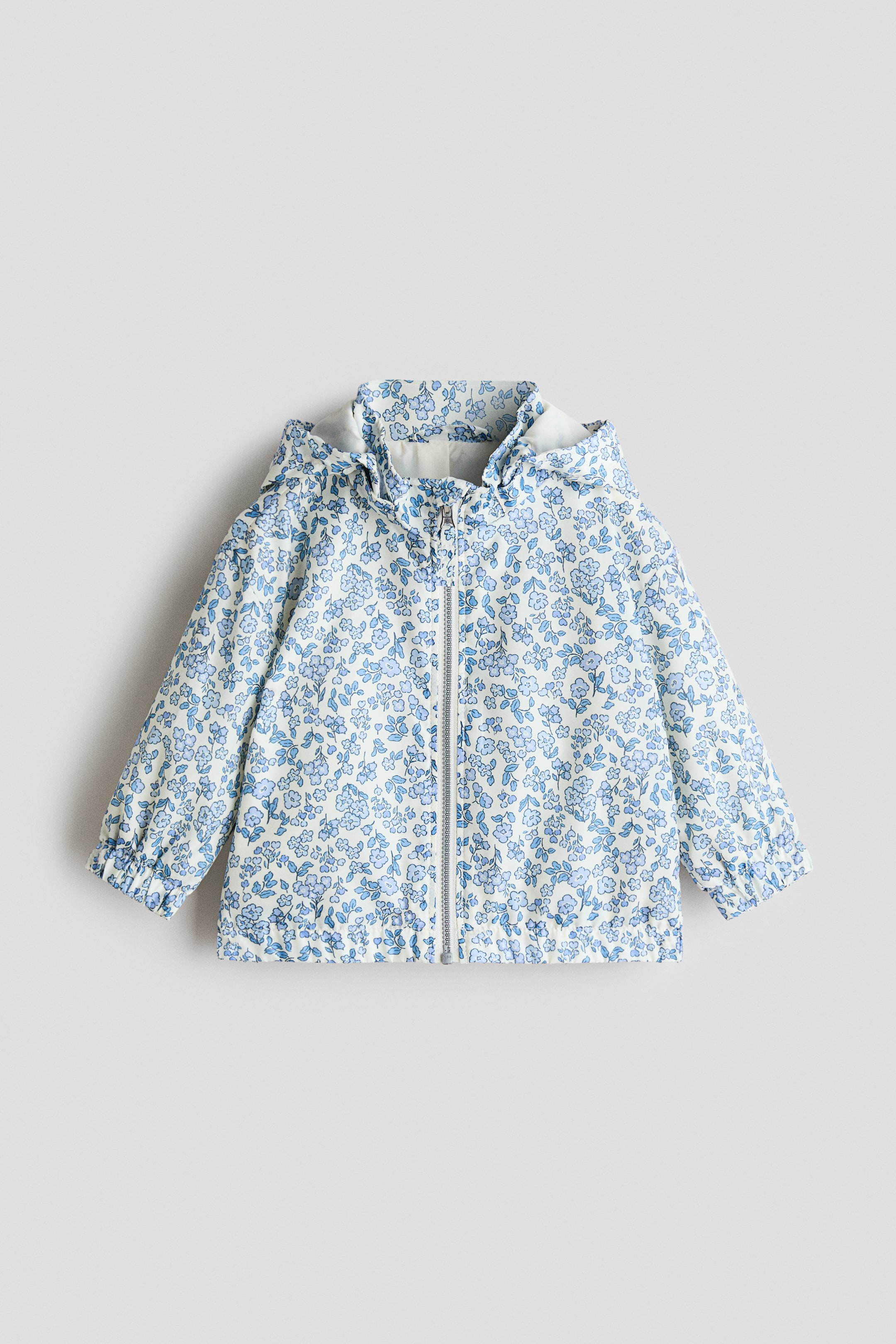 View larger image: Shown from the front, the jacket features a printed weave with a blue floral pattern. It is styled with a detachable hood with covered elastication, a stand‑up collar, a front zip, dropped shoulders and covered elastication at the cuffs and hem.