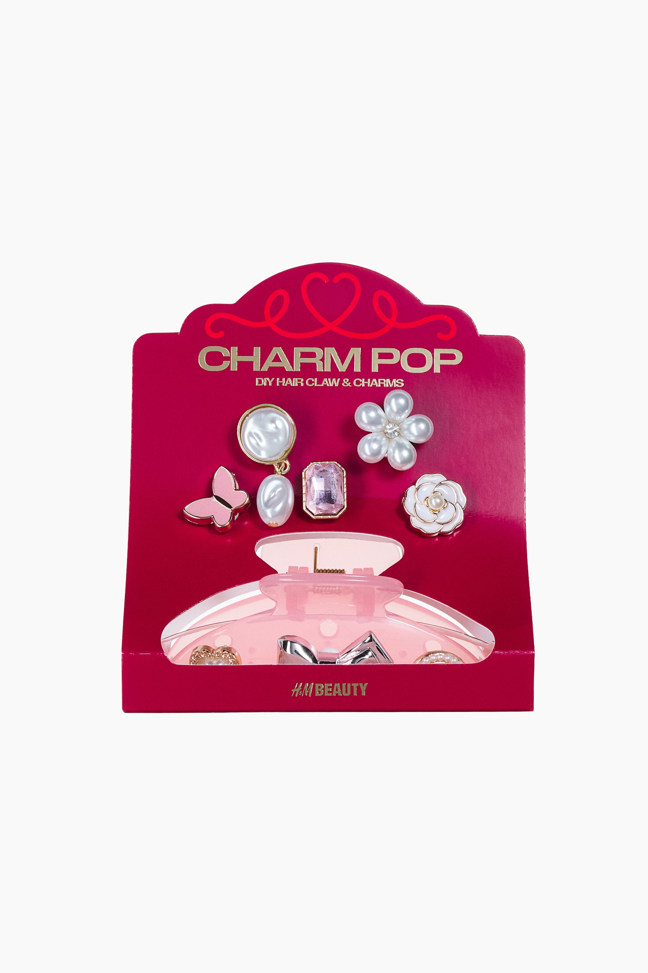Se større billede: Et gør-det-selv-hårklemme- og charms-sæt er vist forfra og præsenterer en halvgennemsigtig pink hårklemme samt fem dekorative charms på et magenta kort. Charmsene omfatter en pink sommerfugl, en hængende perle, en rektangulær pink ædelsten, en perlemorsblomst og en hvid rose.