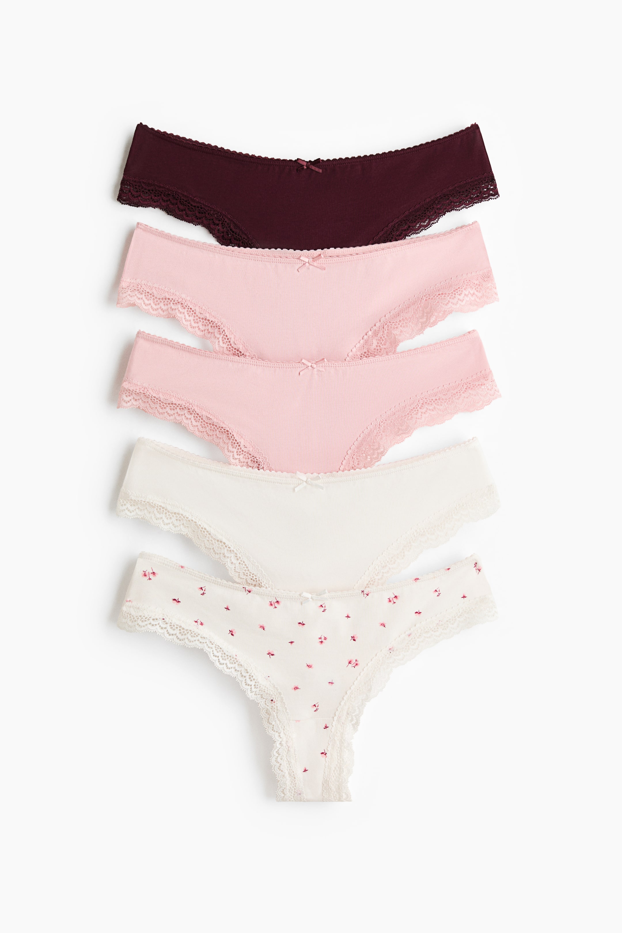 View larger image: Five pairs of Brazilian briefs are neatly stacked, showcasing their front view. Each brief features a low-rise cut with delicate lace trims along the waistband and leg openings, accented by a small bow at the centre front. The briefs come in dark red, light pink, and off-white, with one off-white pair displaying a subtle floral print.
