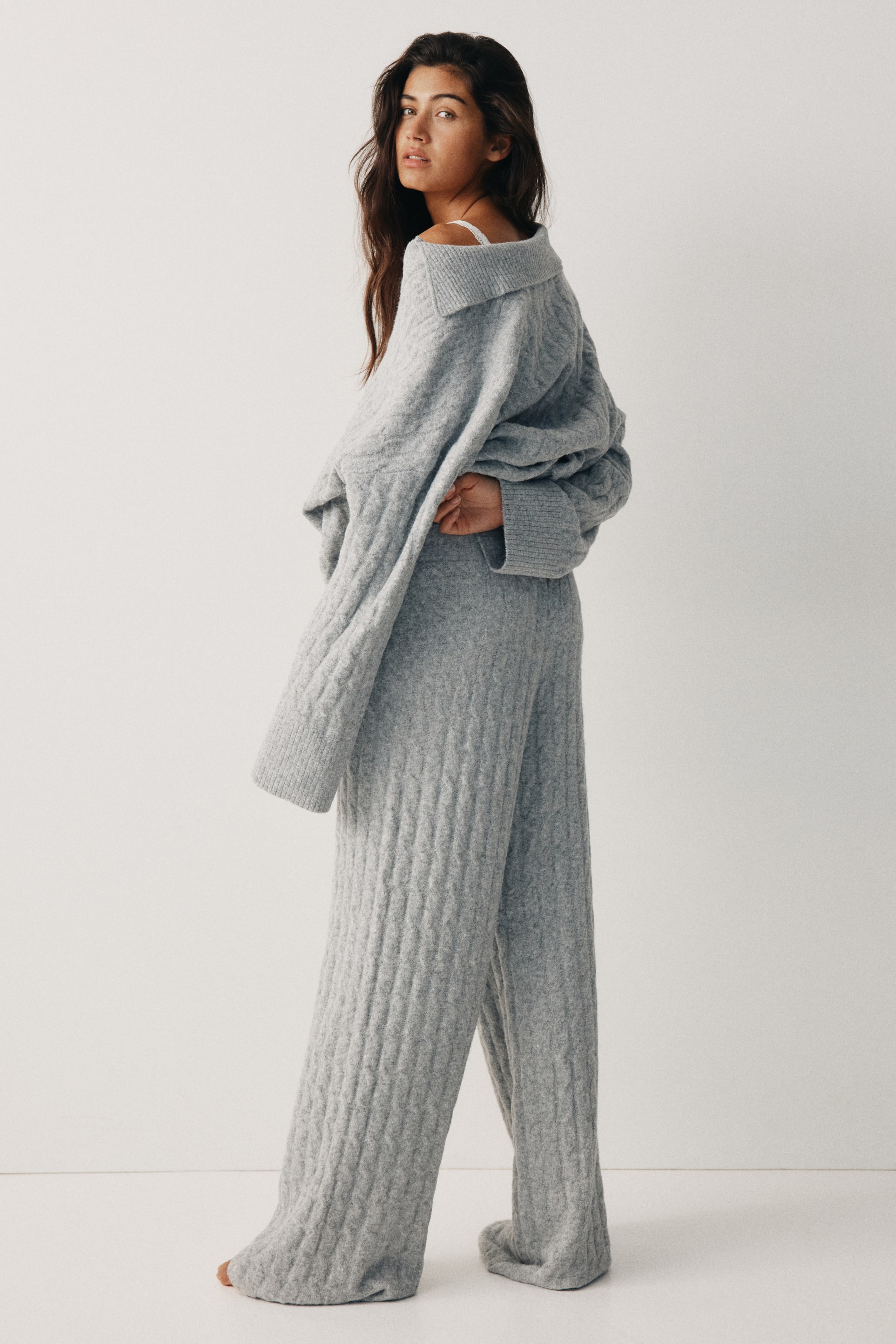 Agrandir l'image: Un ensemble de détente en tricot torsadé gris clair est présenté sous un angle arrière-gauche. Le haut surdimensionné présente un col large et replié ainsi que des poignets côtelés, tandis que le pantalon à jambes larges assorti affiche un motif en tricot torsadé cohérent.