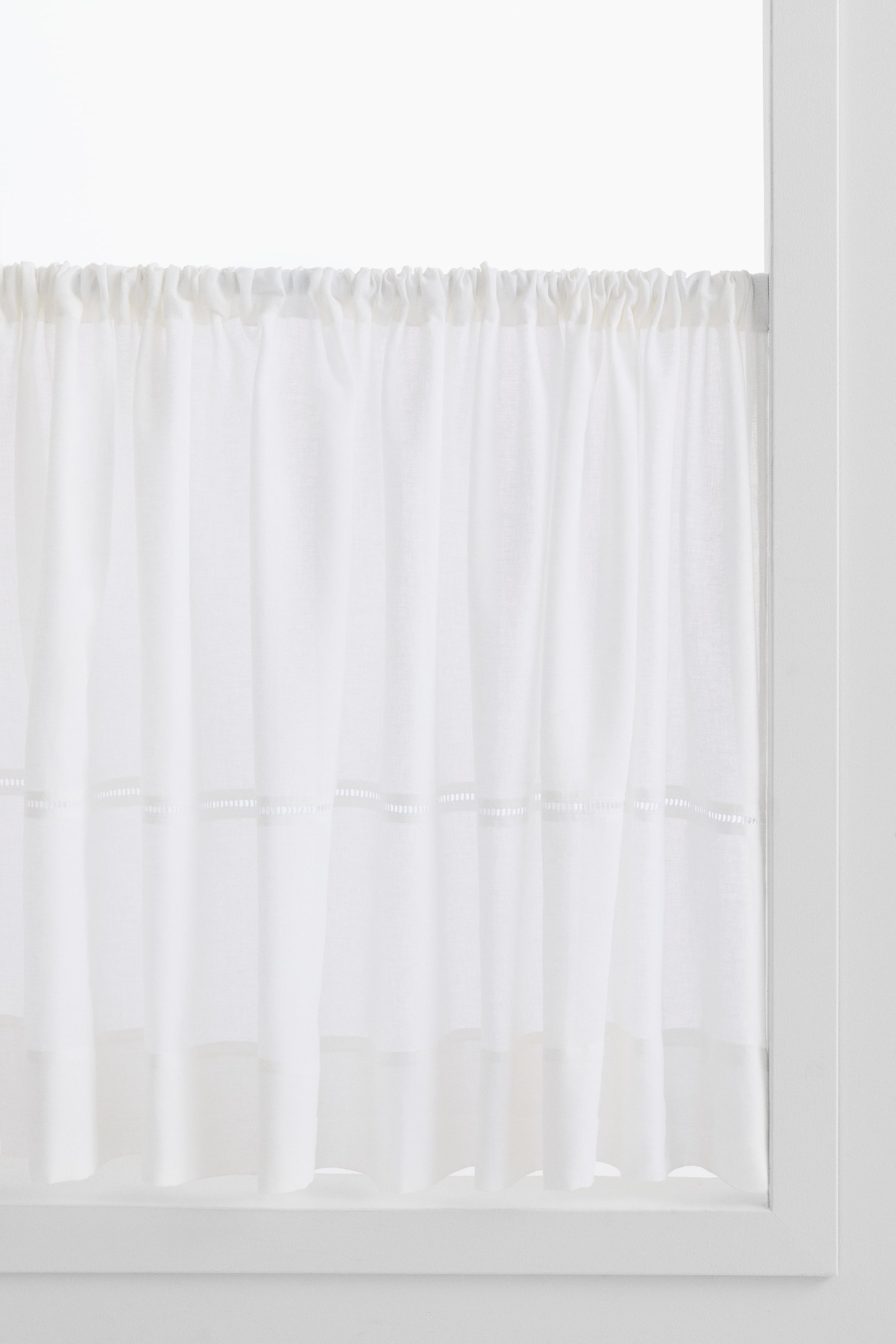Ver imagen más grande: Una cortina de tela blanca translúcida se muestra de frente, con un borde superior fruncido ensartado en una barra. Dos bandas horizontales de detalles calados son visibles a lo largo de su ancho, situadas por encima del dobladillo inferior recto.